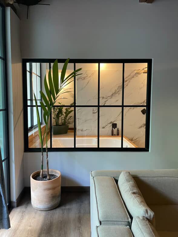 Habitación con gran ventanal que da a un baño con pared de mármol y bañera.