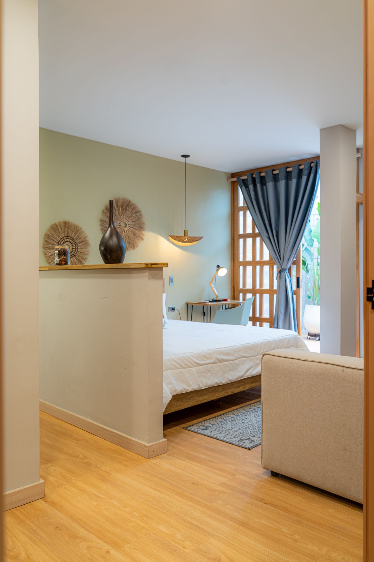 Dormitorio con pisos de madera clara, cama, escritorio y cortinas azules.