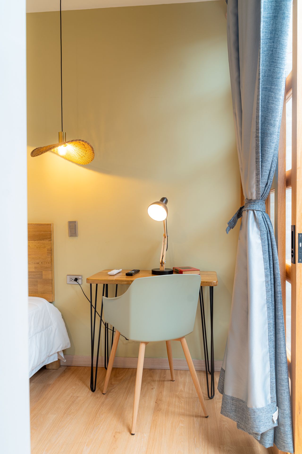 Escritorio con silla en la habitación; lámpara de escritorio encendida; ventana con cortina en el marco; luz colgante.