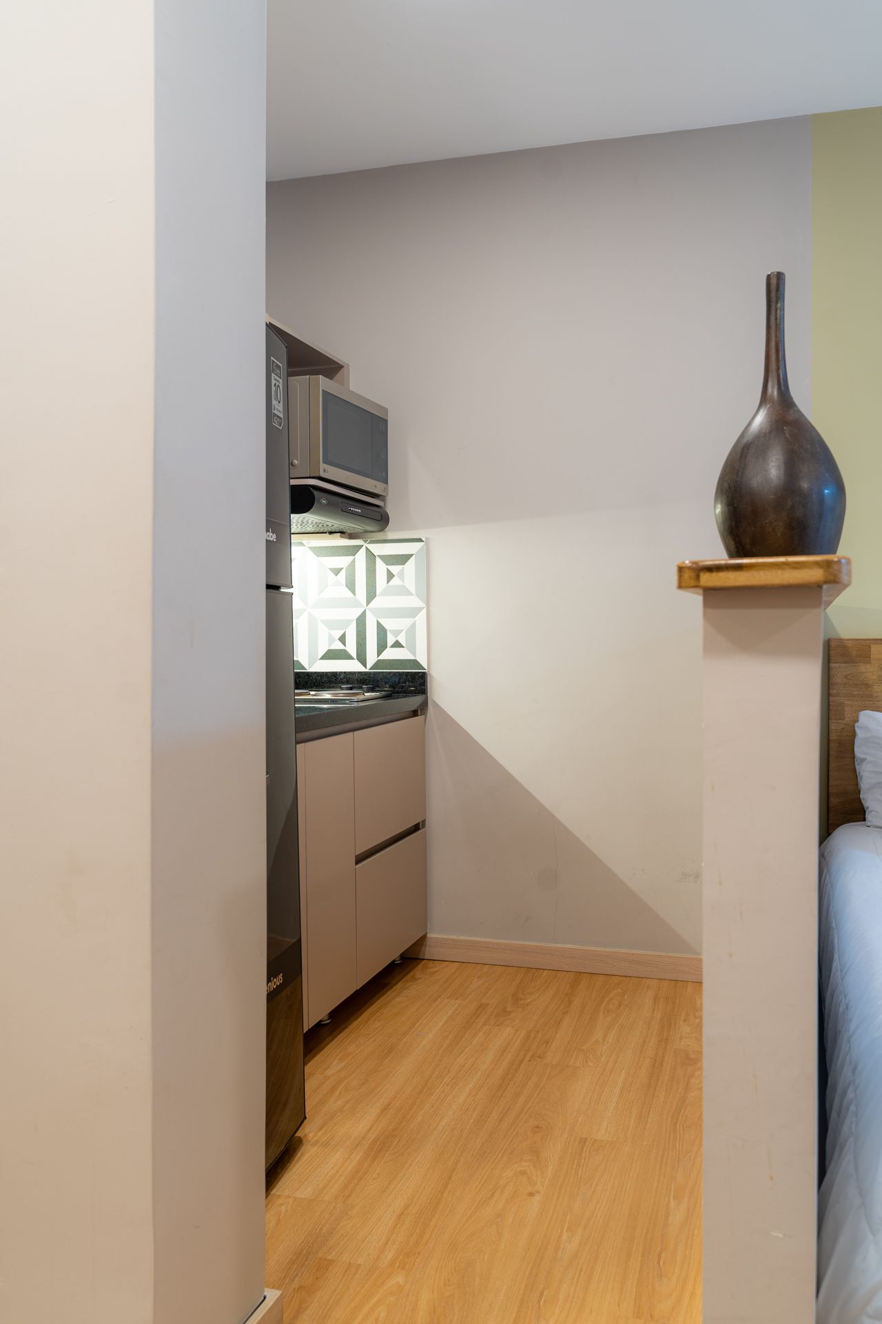 Pequeña área de cocina con pisos de apariencia de madera, gabinetes de color beige, microondas y refrigerador.