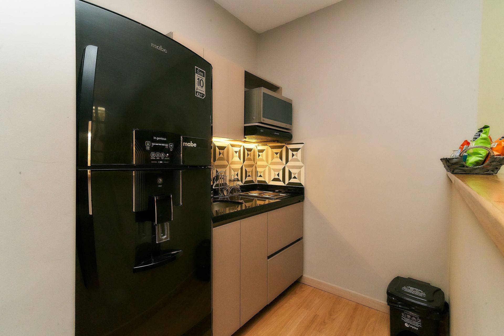 Refrigerador negro en una cocina pequeña con microondas, gabinetes y un bote de basura.