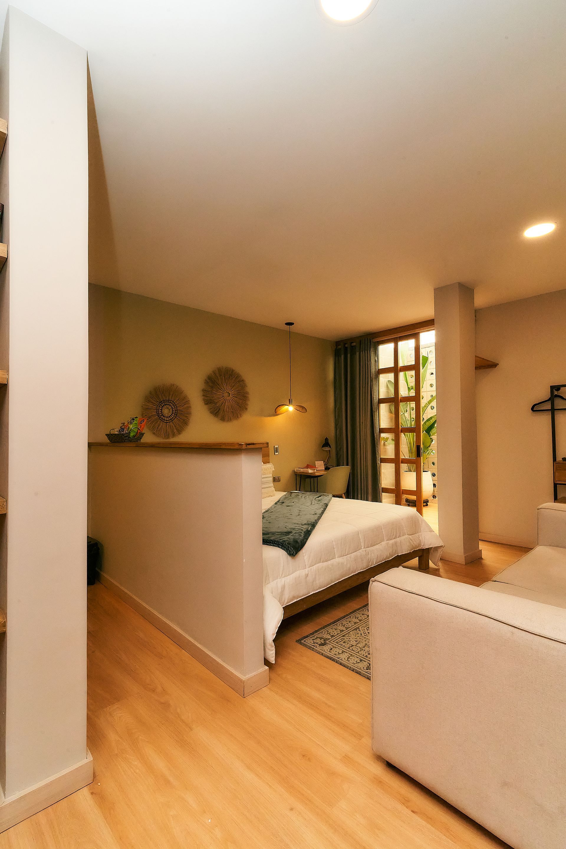 Dormitorio con cama, sofá y puerta a patio, con paredes de colores claros y suelos de madera.