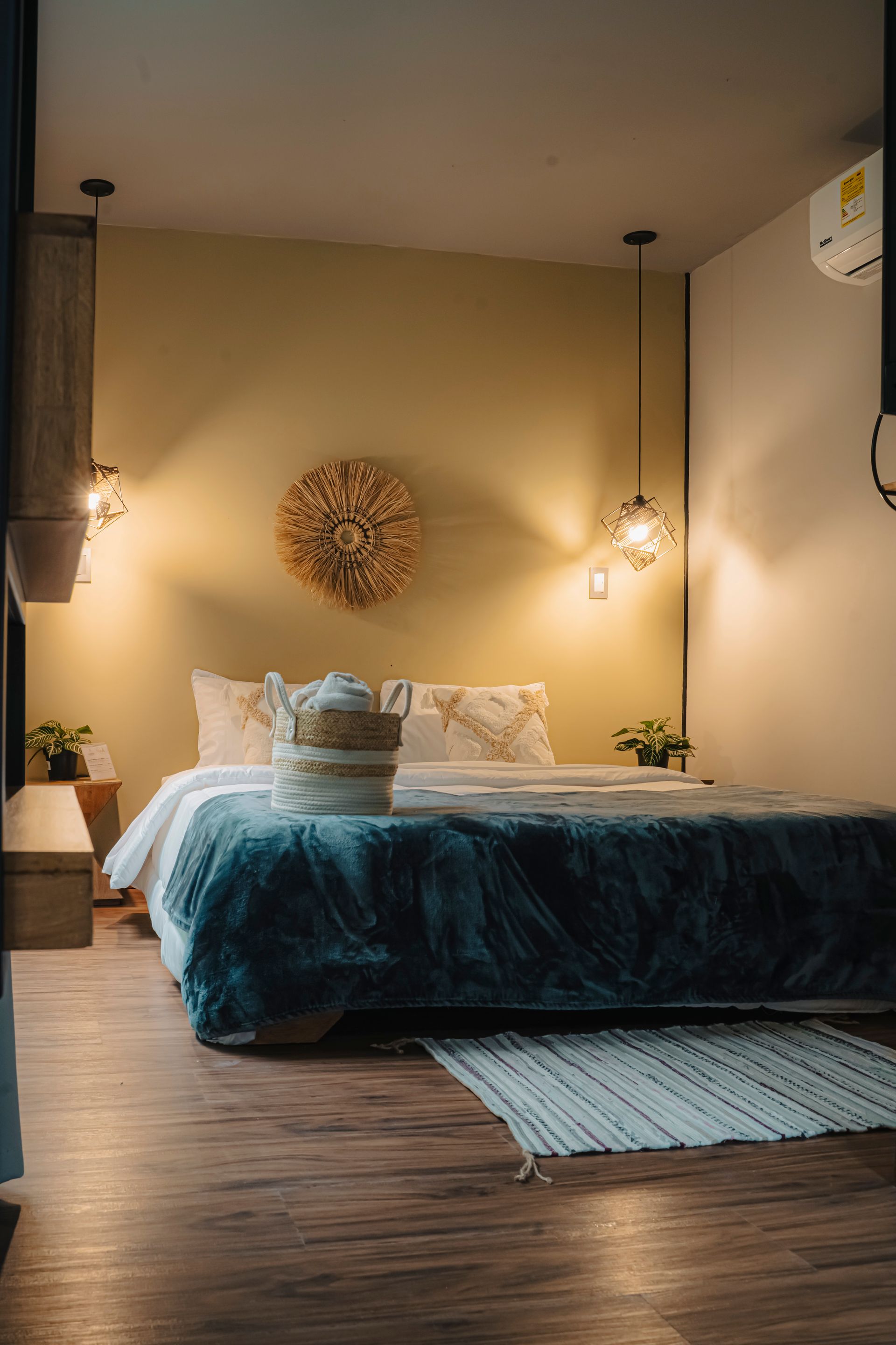 Dormitorio acogedor con cama, manta, almohadas, alfombra y decoración mural. Iluminación cálida. Suelo de madera.