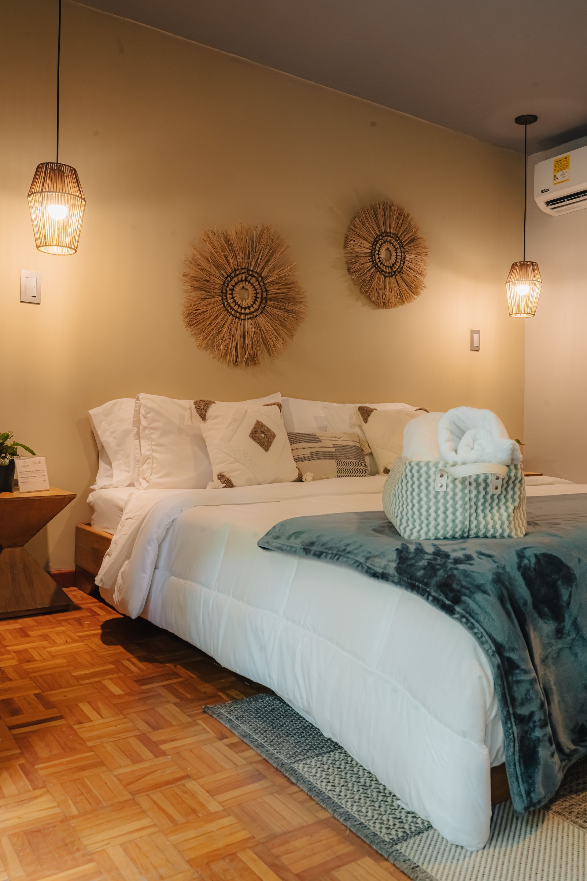 Dormitorio con una cama, dos lámparas colgantes, decoración de pared tejida y piso de madera.