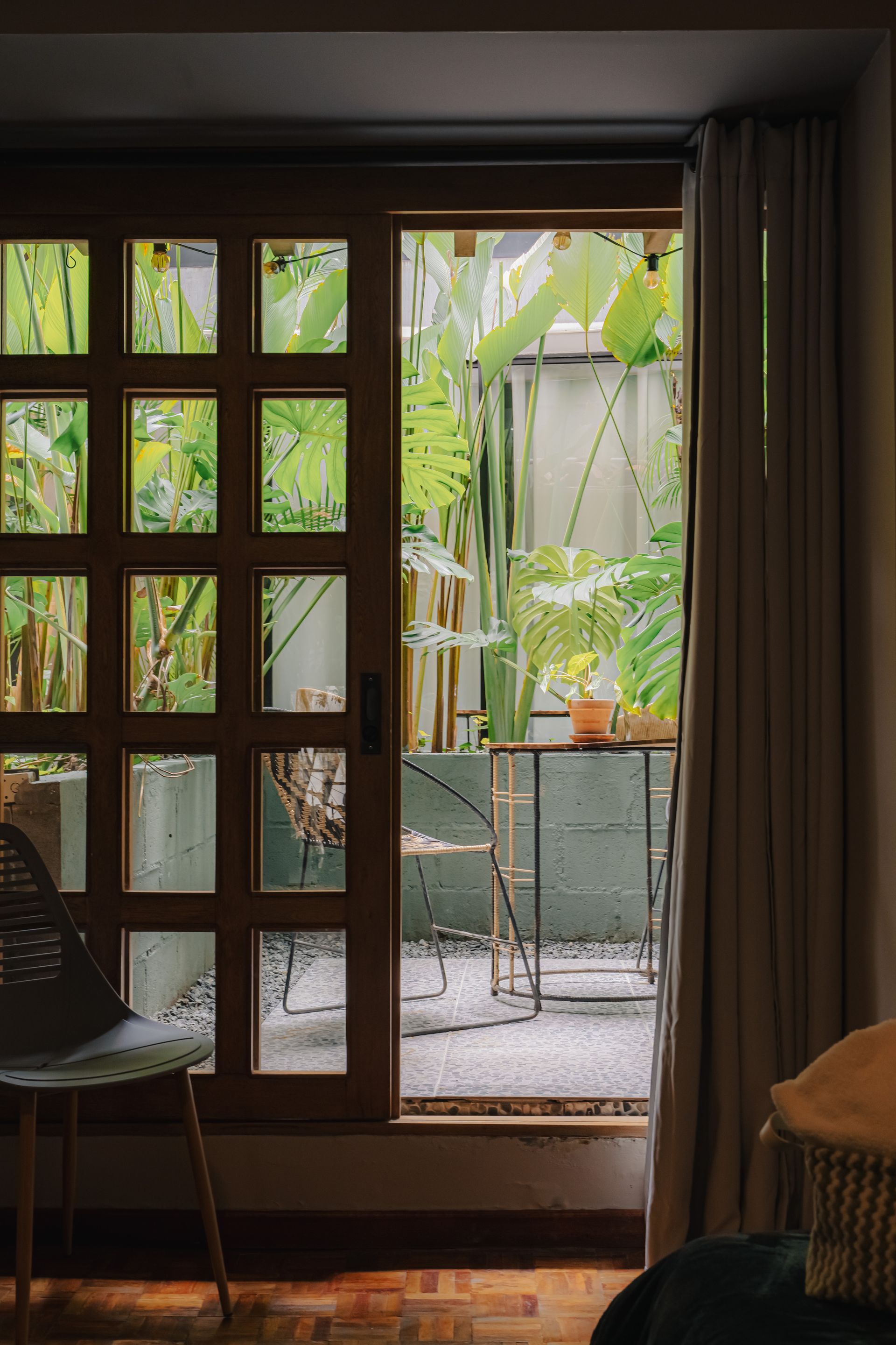 Puerta de madera abierta a un exuberante patio con jardín con mesa y sillas.
