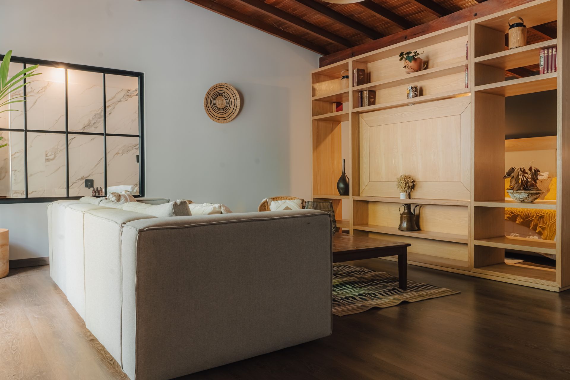 Sala de estar con un sofá gris claro, estanterías empotradas de madera, pisos de madera oscura y una ventana.