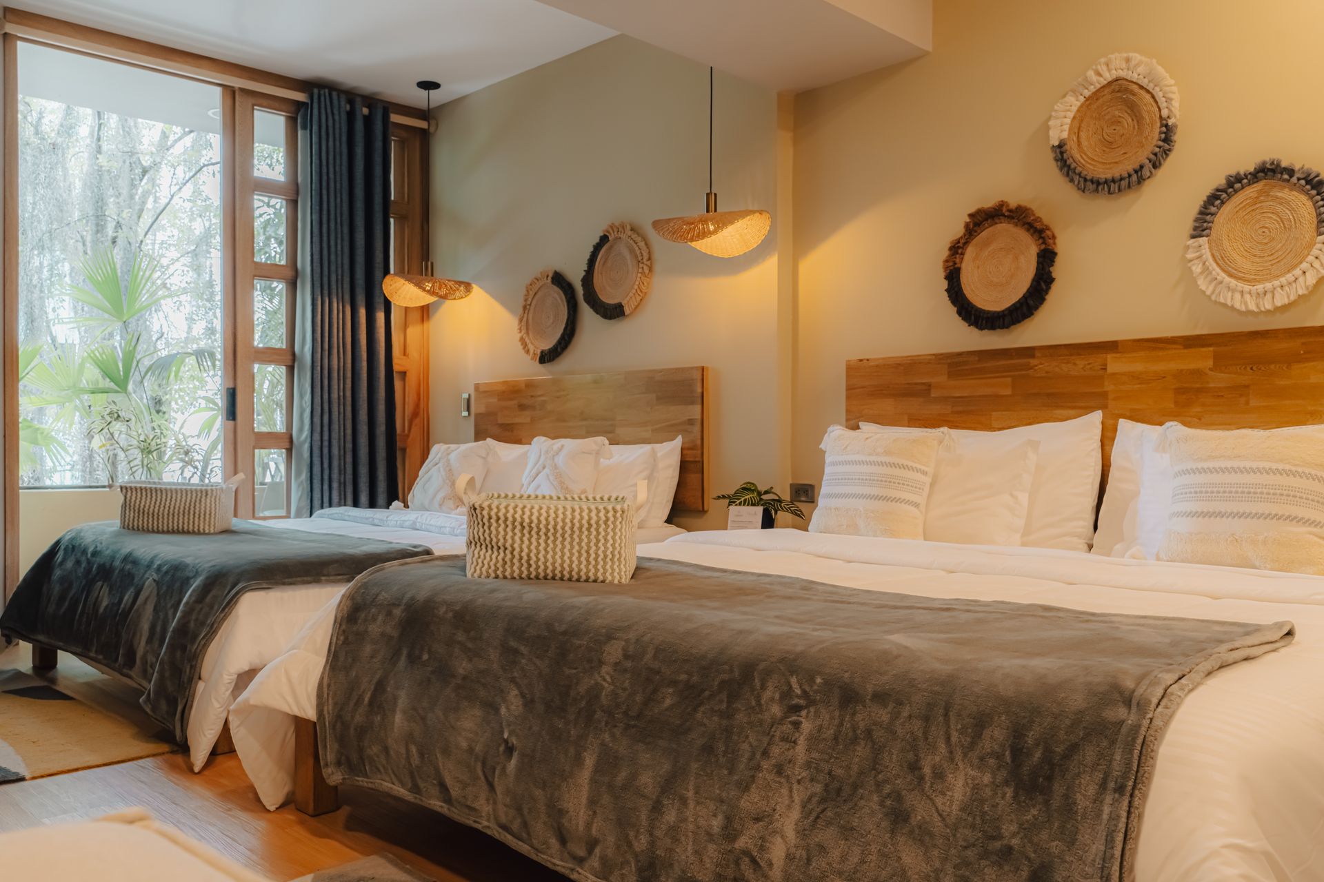 Dormitorio de hotel con dos camas queen, cestas decorativas en la pared y ventana grande.