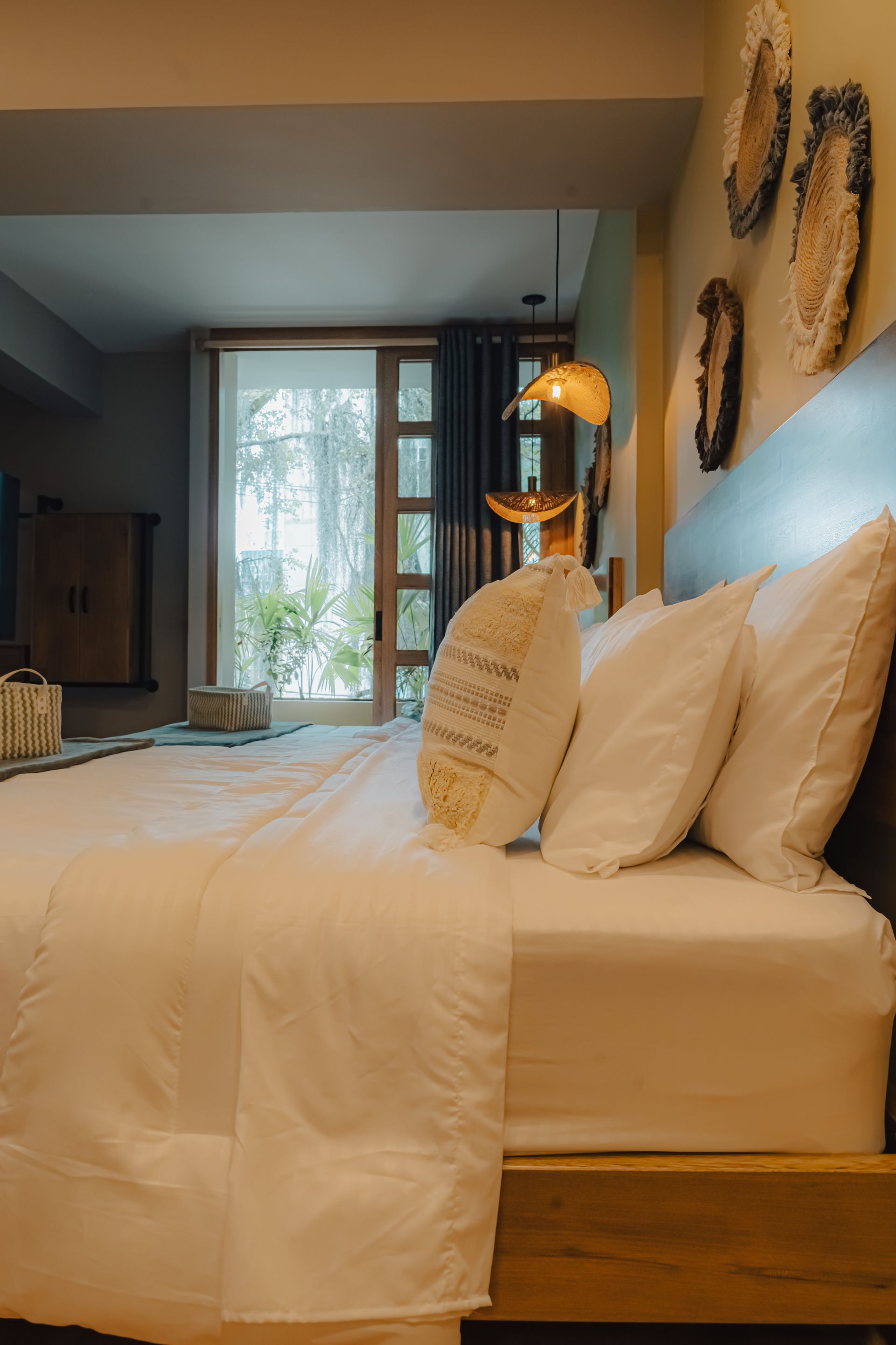 Acogedor dormitorio con ropa de cama blanca, cabecero de madera y arte decorativo en la pared. Vista de una ventana.