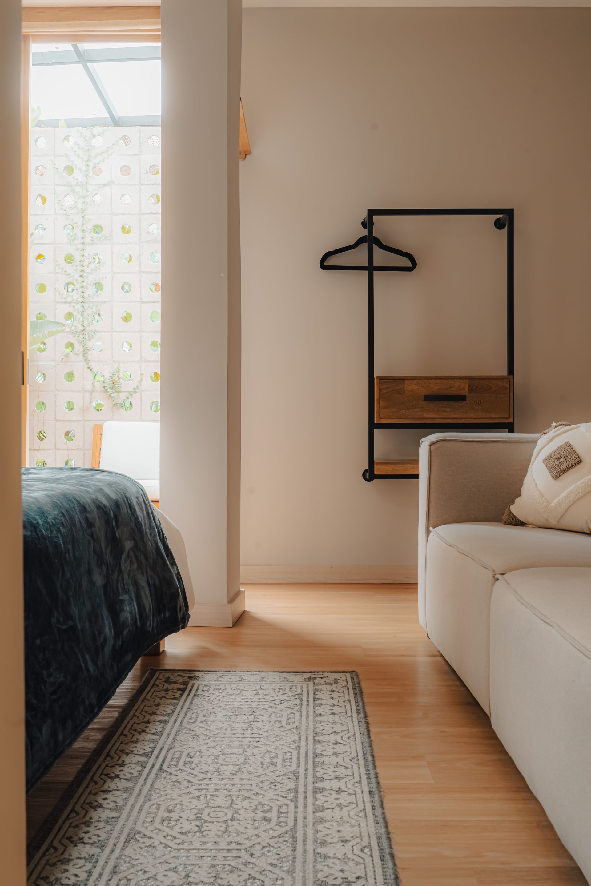 Interior de dormitorio con cama, sofá y perchero cerca de una ventana.