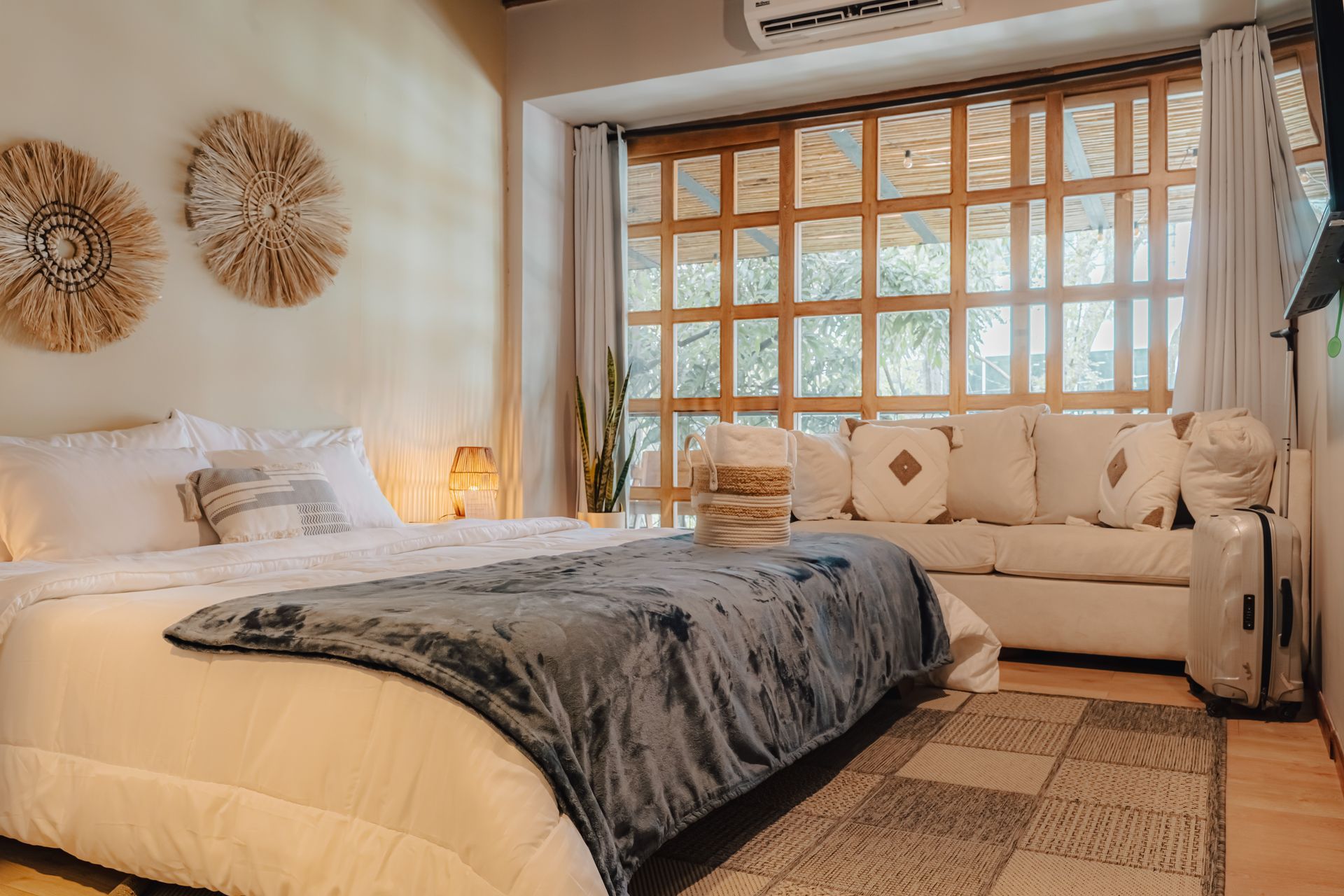 Dormitorio con cama, sofá, ventanal, decoración de pared tejida, colores neutros.