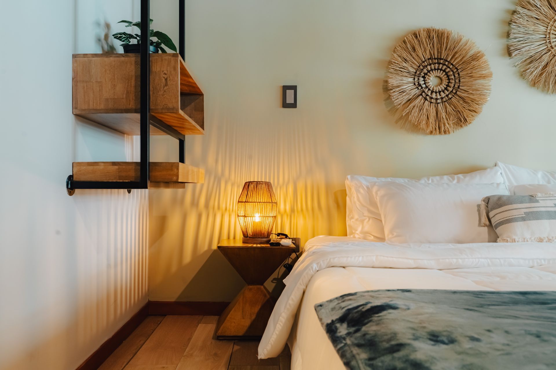 Rincón de dormitorio con cama, mesita de noche, estantería y adornos de pared.