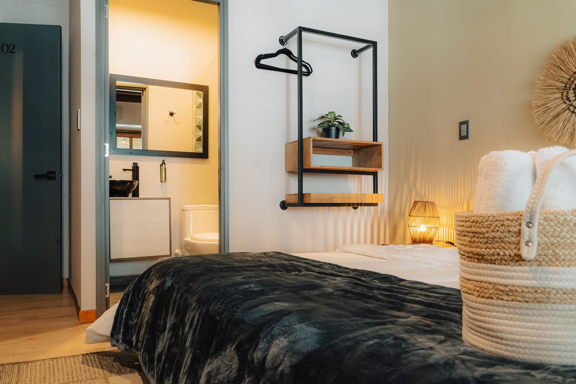 Interior de dormitorio con cama, armario abierto y vista de un baño. Tonos neutros y texturas naturales.