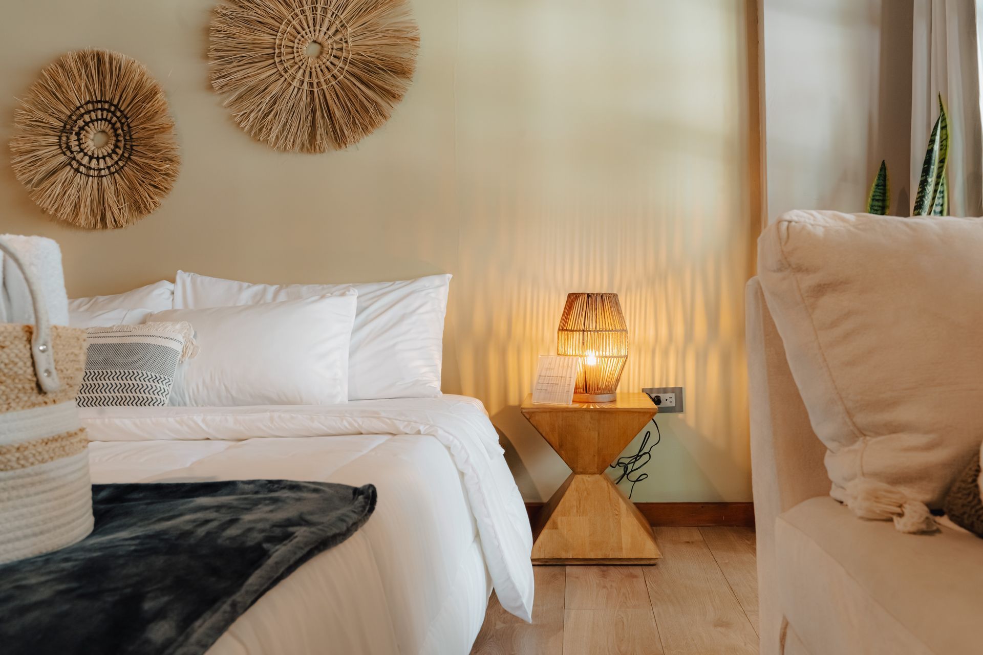 Dormitorio con ropa de cama blanca, mesita de noche de madera y tapices decorativos.