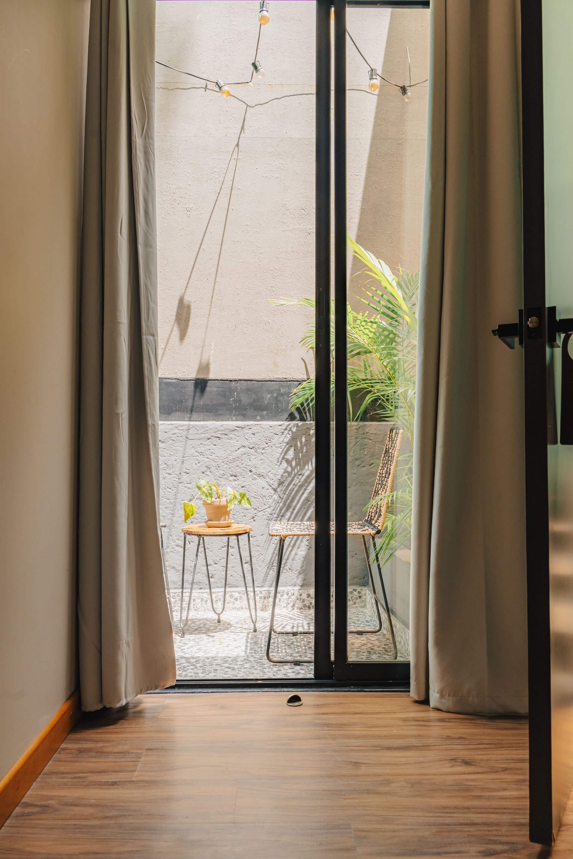 Entrada a un pequeño patio. Dos sillas y una mesa se encuentran afuera, iluminadas con guirnaldas de luces.