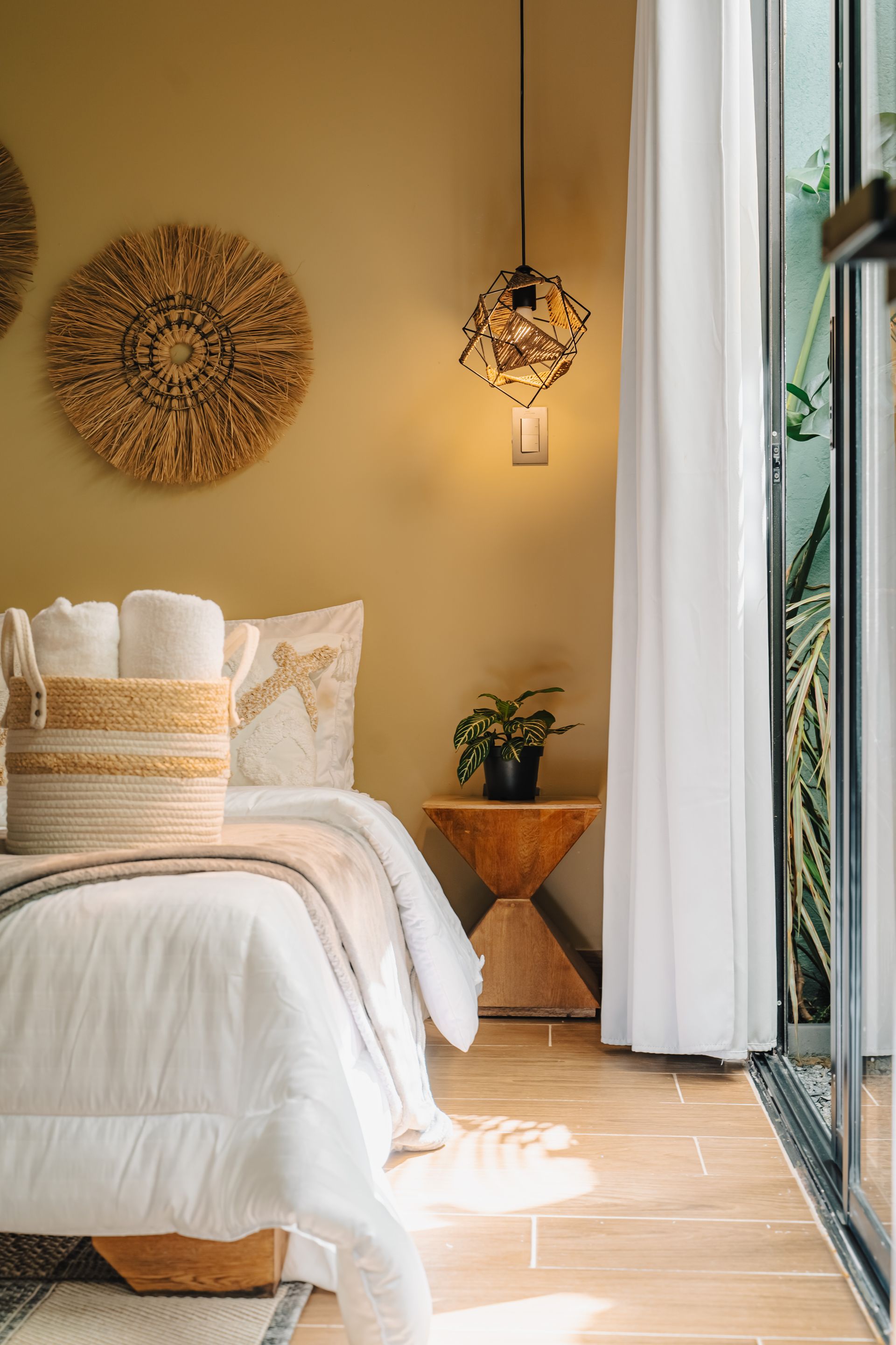 Dormitorio con ropa de cama blanca, decoración de pared tejida y una lámpara colgante.