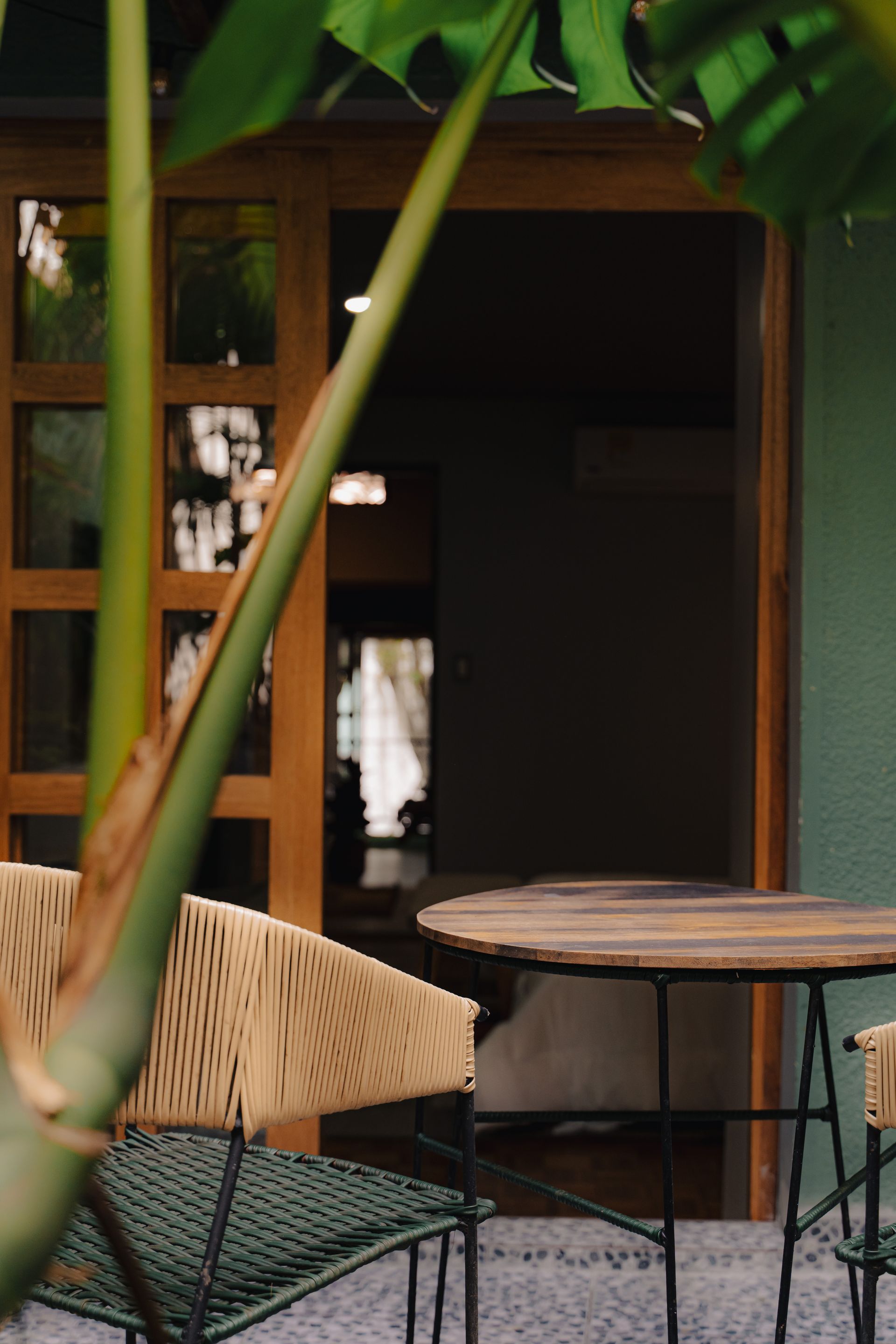Cafetería al aire libre con mesa de madera y silla tejida frente a una puerta.