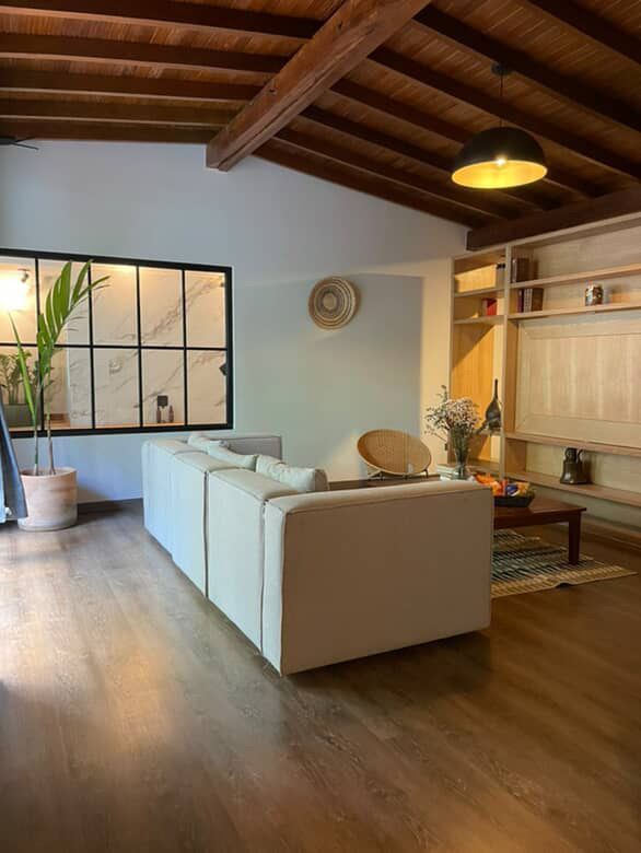 Sala de estar con sofá blanco, vigas de madera, estanterías empotradas, gran ventanal.