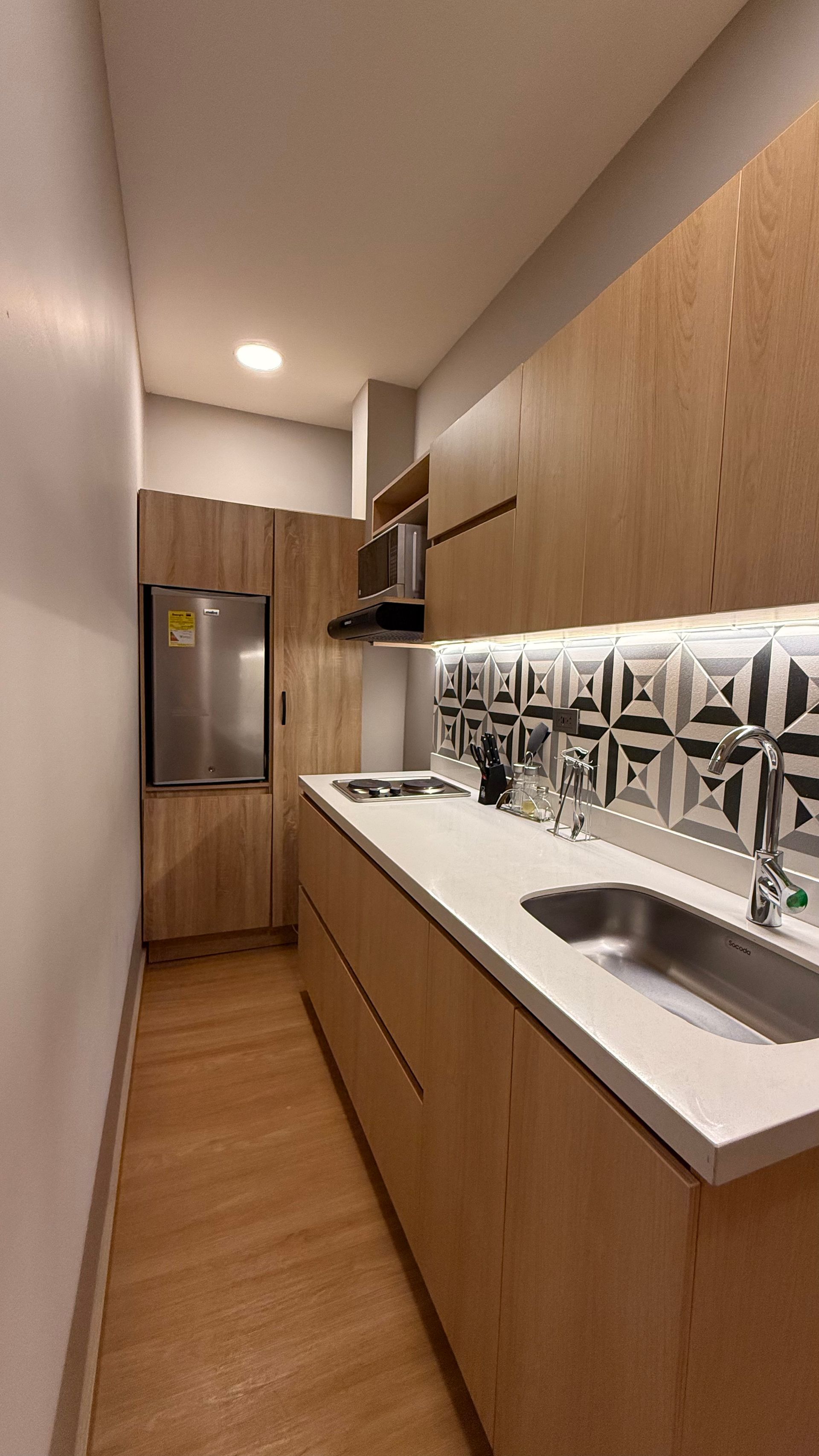 Cocina moderna con gabinetes de madera clara, encimeras blancas y protector contra salpicaduras estampado.