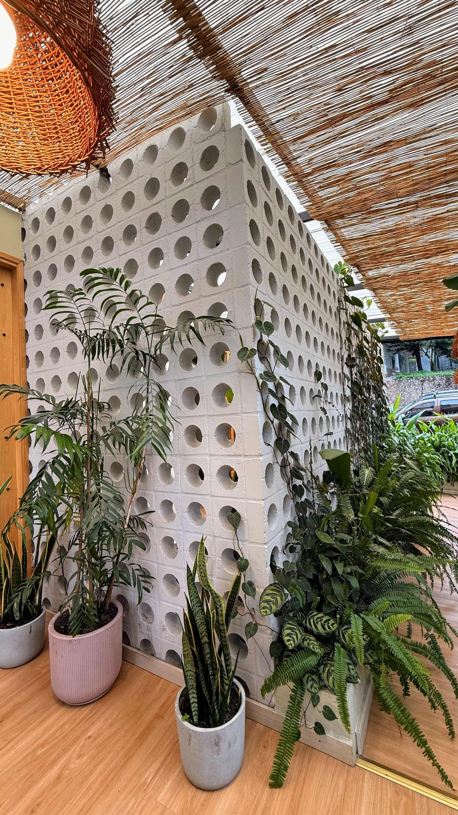 Pared de ladrillo blanco perforado con plantas en macetas en ambiente exterior.