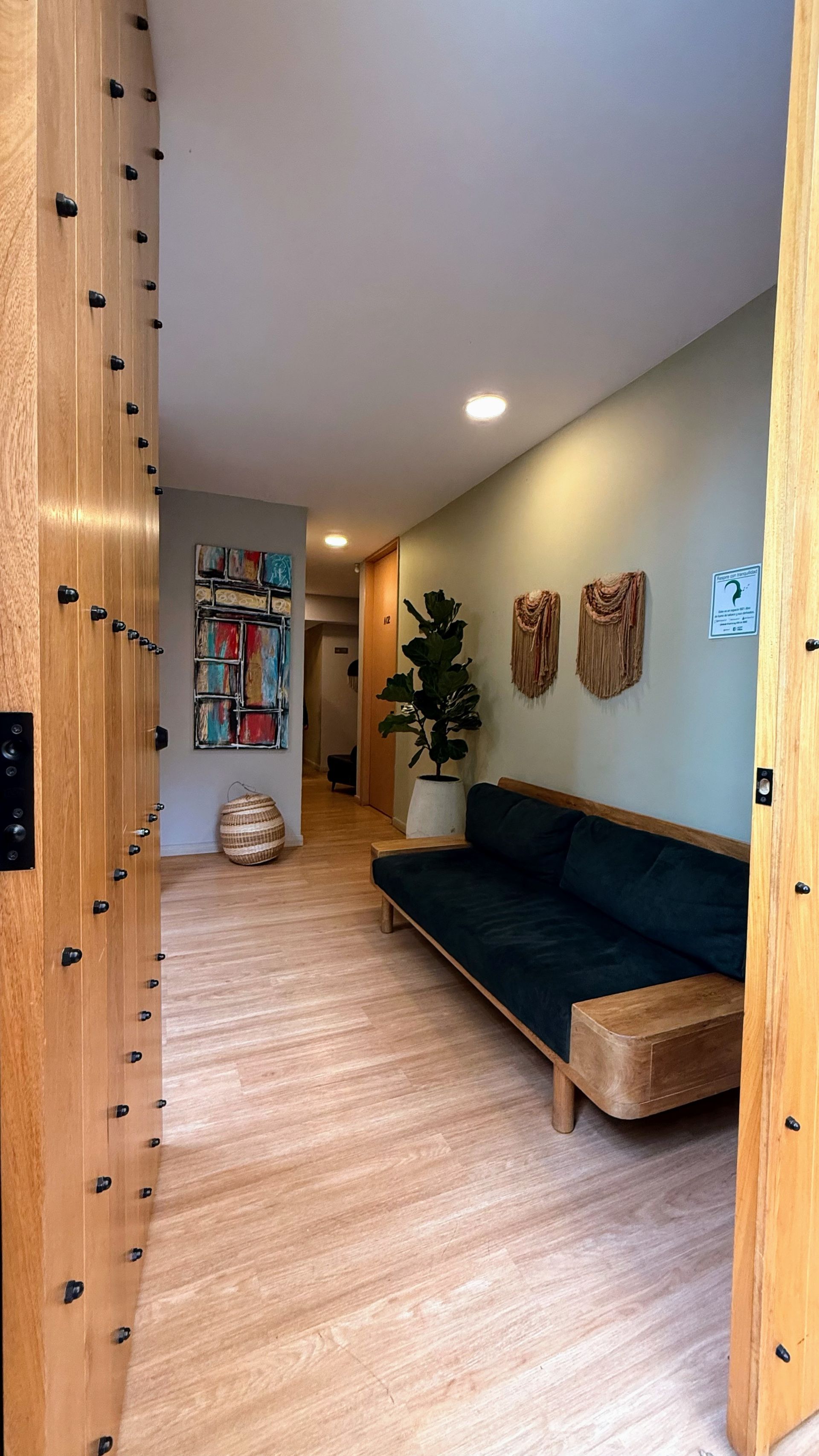 Entrada de madera con sofá oscuro, planta, arte y paredes claras.