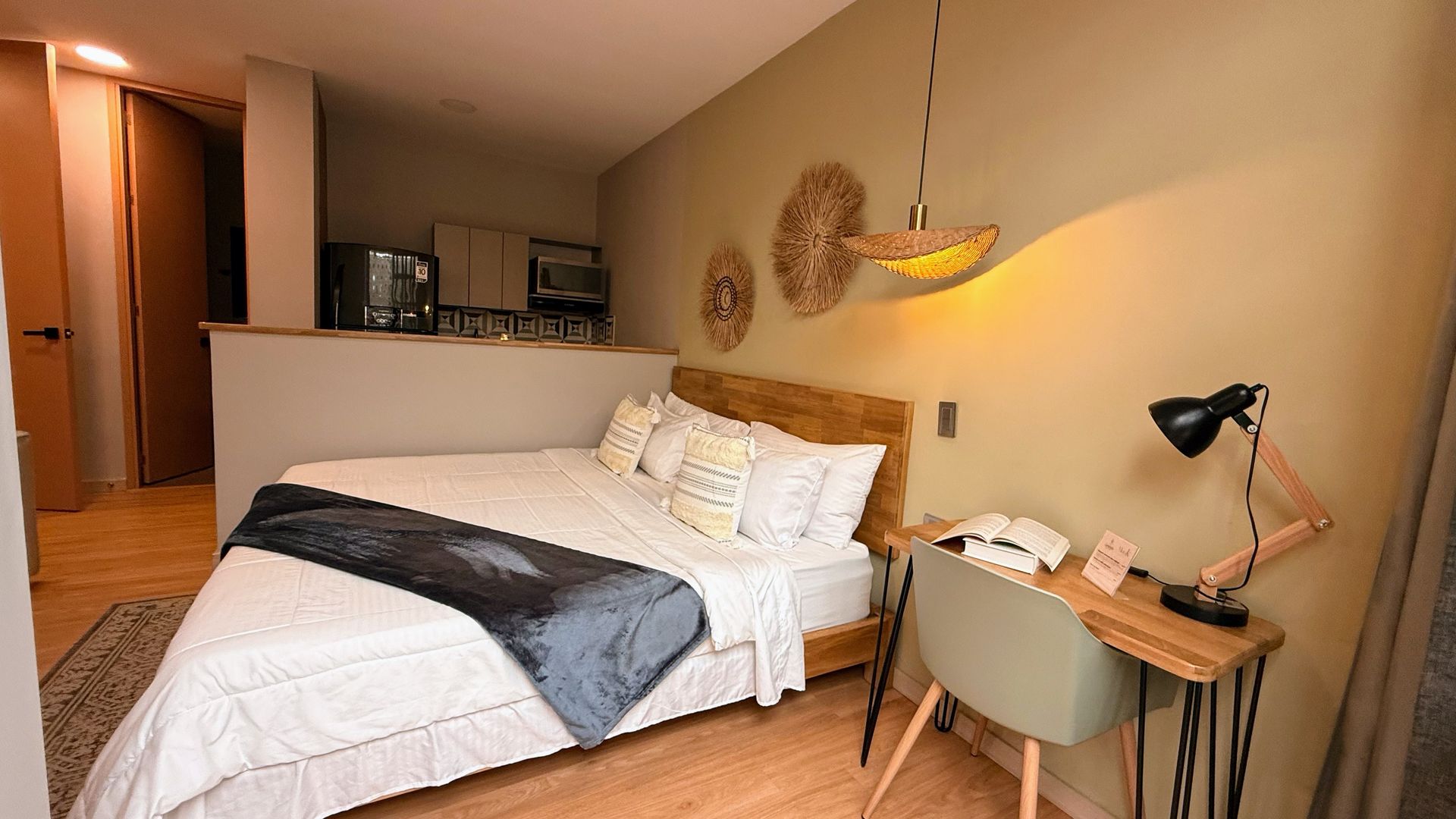 Dormitorio con cama doble, escritorio y pequeña cocina. Decoración en tonos verdes y blancos.