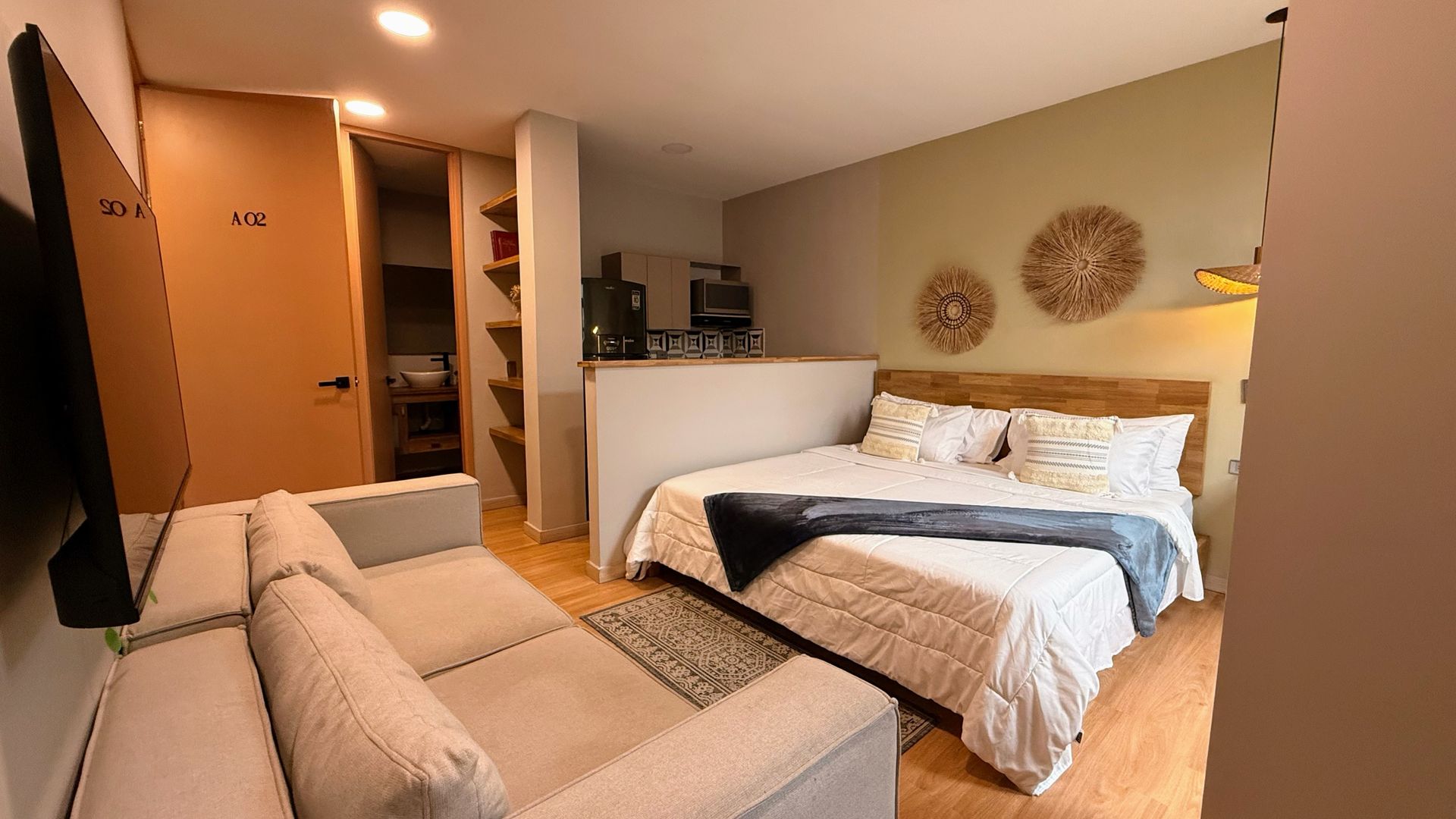 Pequeño apartamento tipo estudio con cama, sofá, cocina americana y detalles de madera.