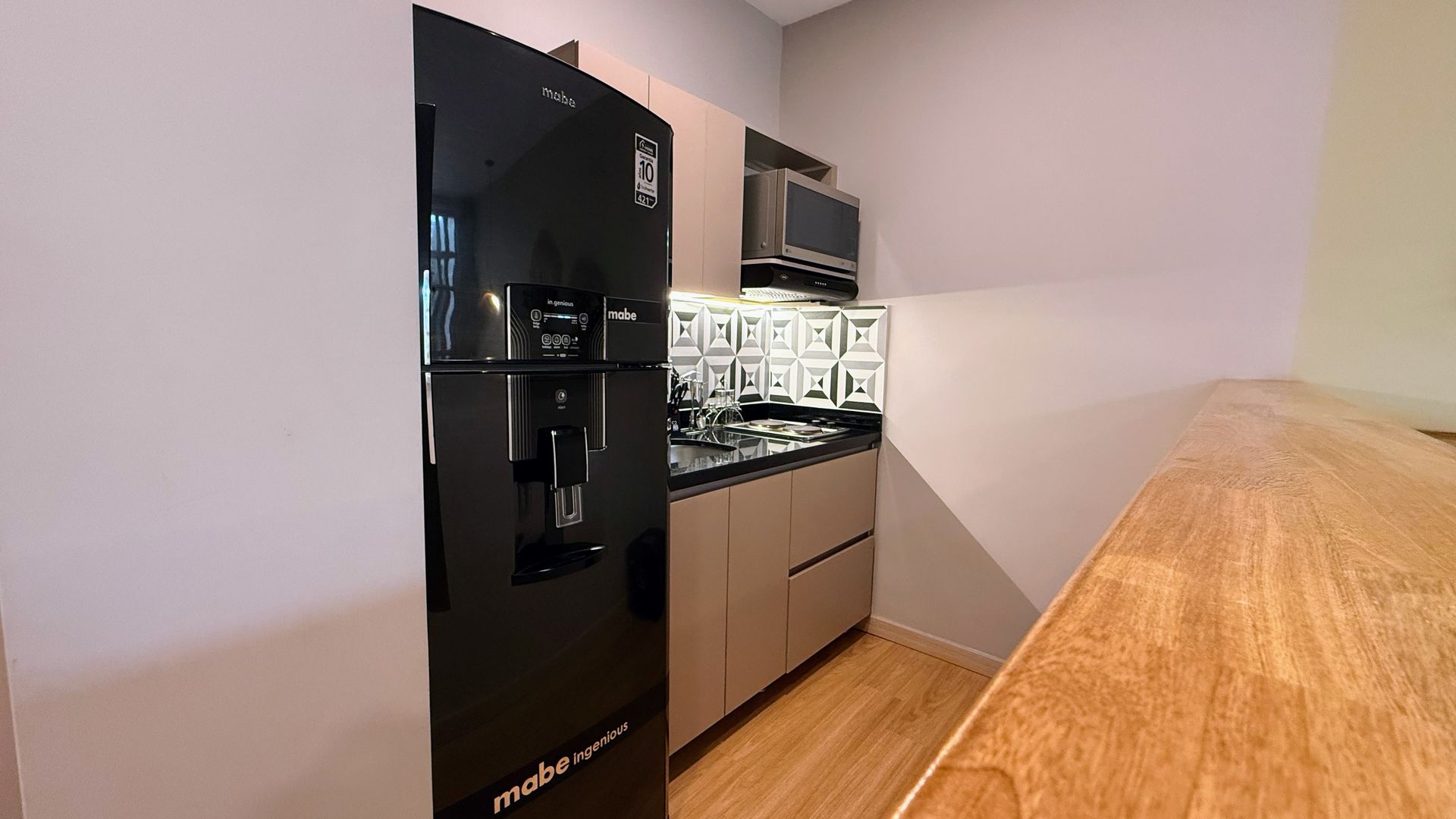 Refrigerador negro en una cocina pequeña con gabinetes de color marrón claro y una encimera de madera.