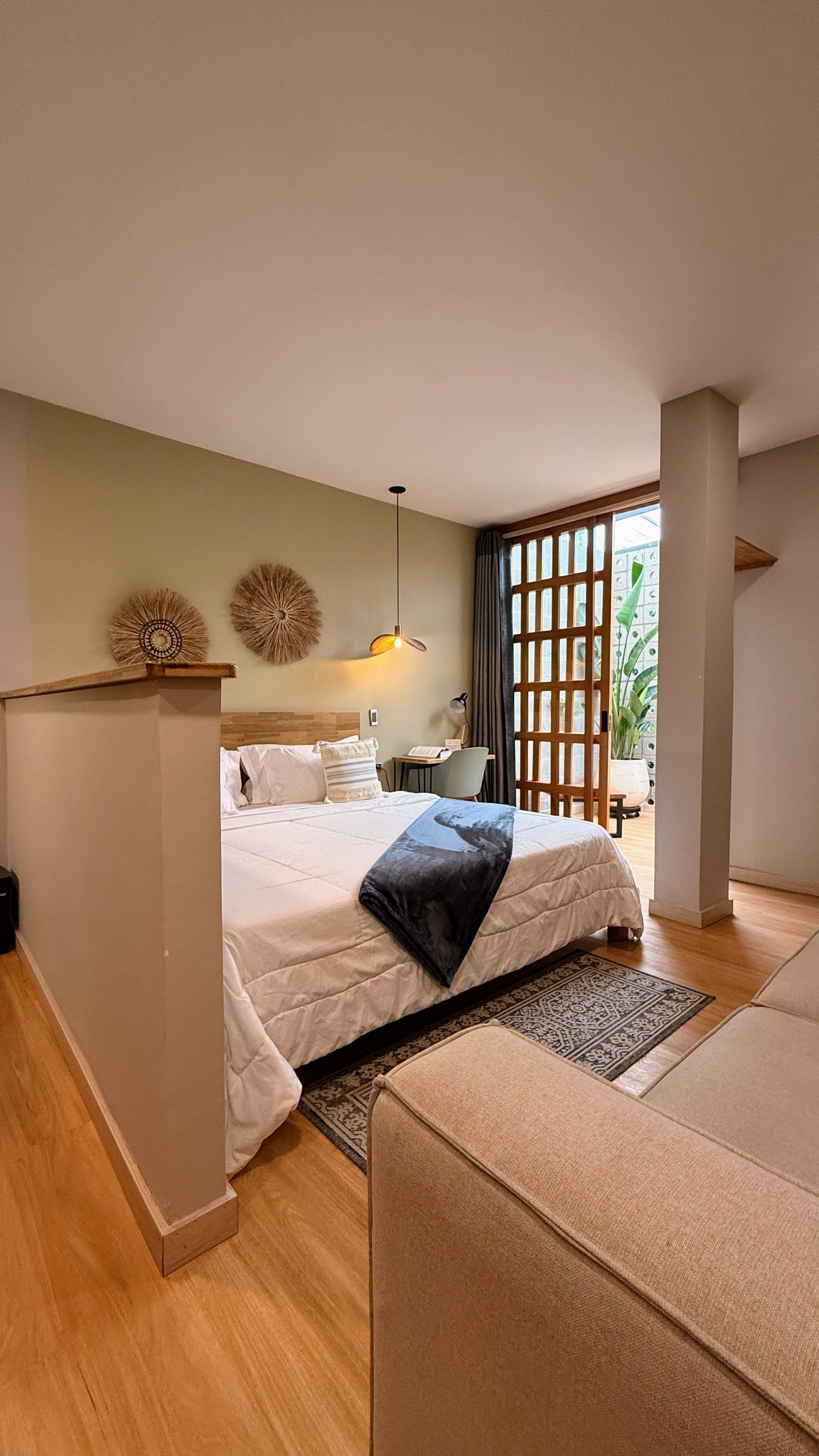 Dormitorio con cama, sofá y acceso a patio, con luz natural y tonos neutros.