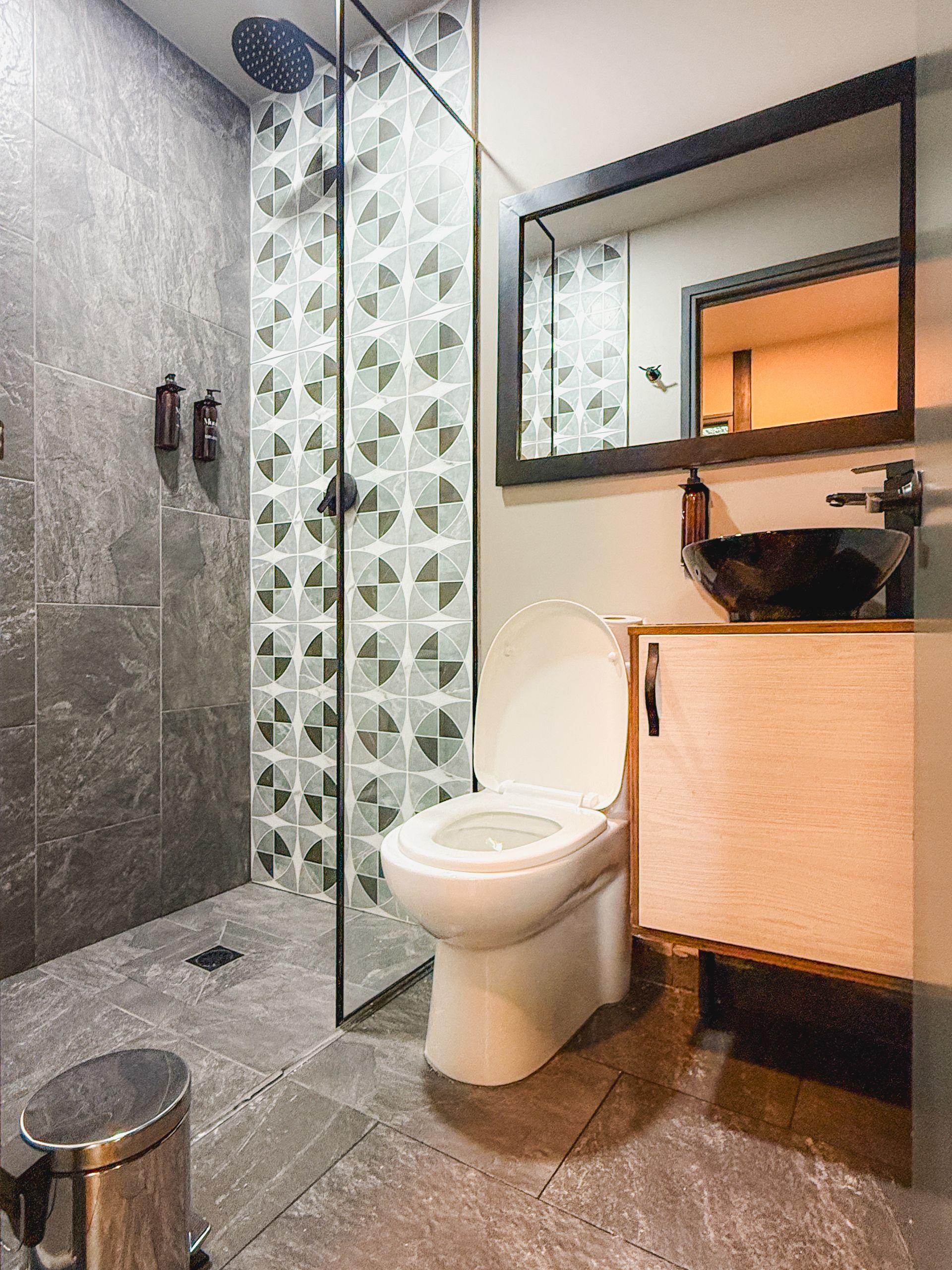 Baño moderno con paredes de azulejos grises, ducha, inodoro y tocador de madera.