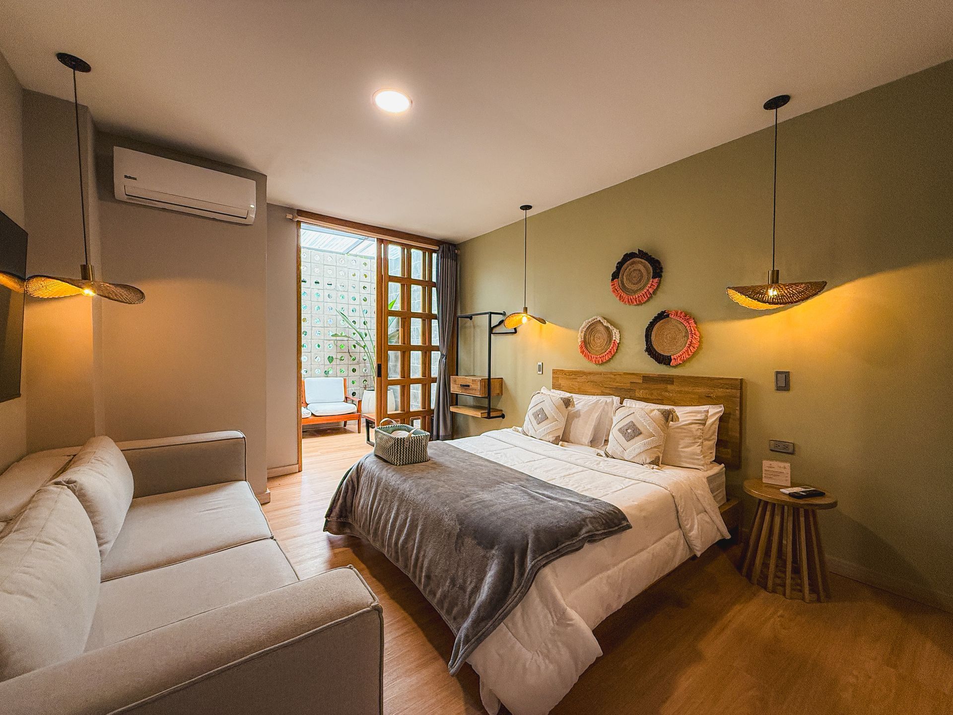 Acogedora habitación de hotel con cama, sofá y puerta abierta a una zona de estar al aire libre. Colores tierra.