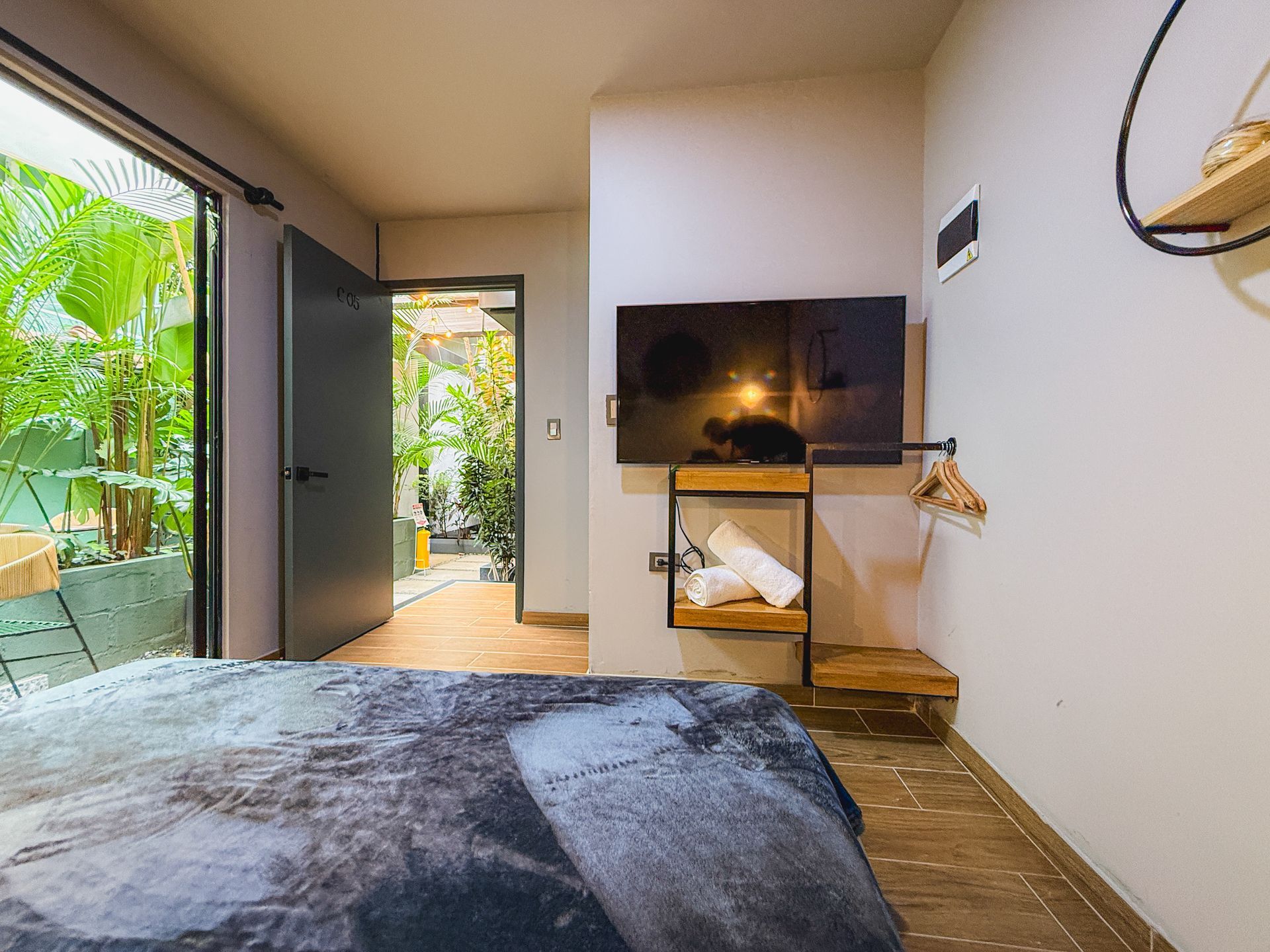 Recámara con puerta abierta a patio, TV en pared, decoración minimalista, tonos grises y madera.