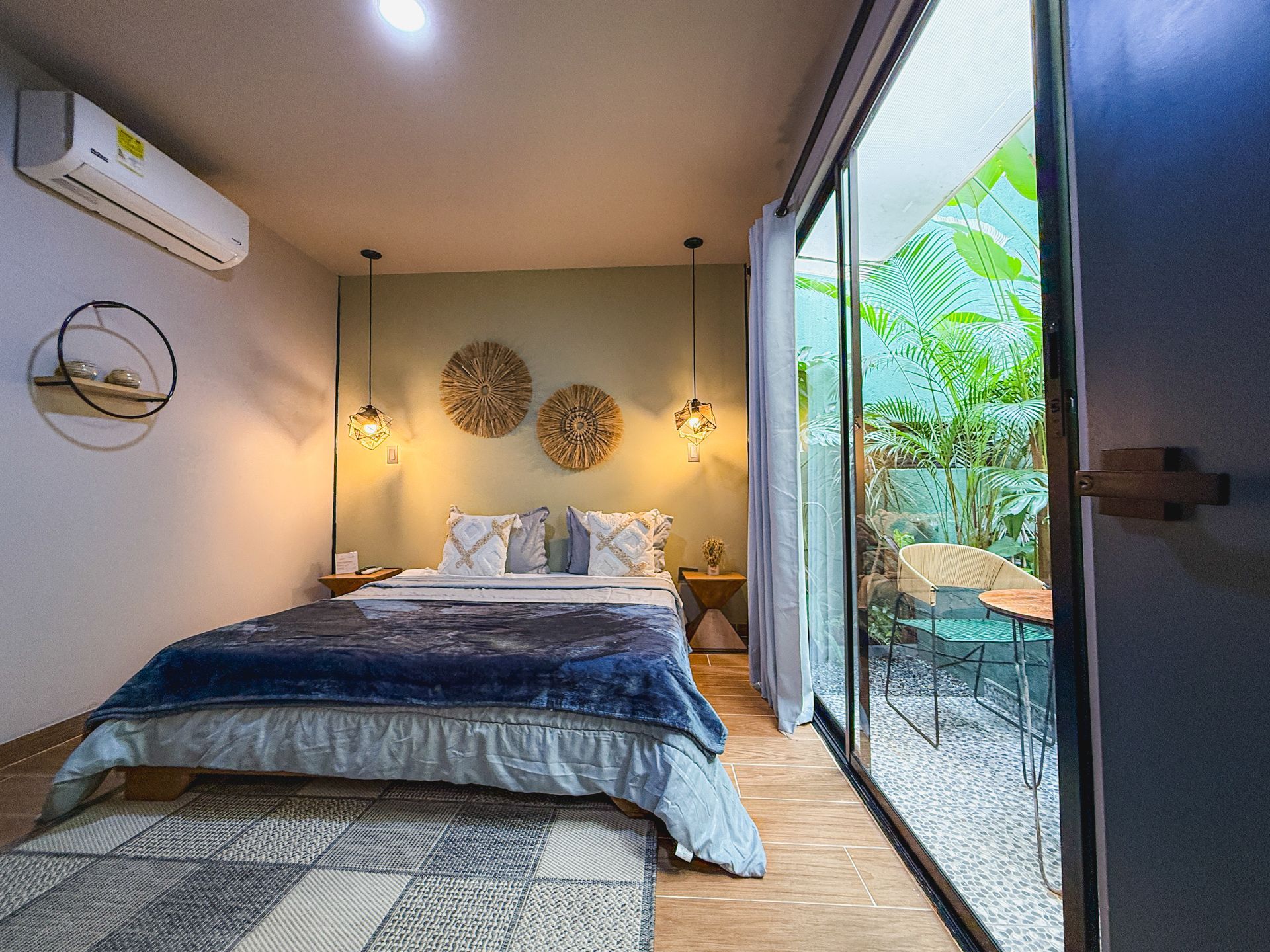 Dormitorio con gran puerta corrediza de vidrio, una cama con manta azul y vista a un patio al aire libre.