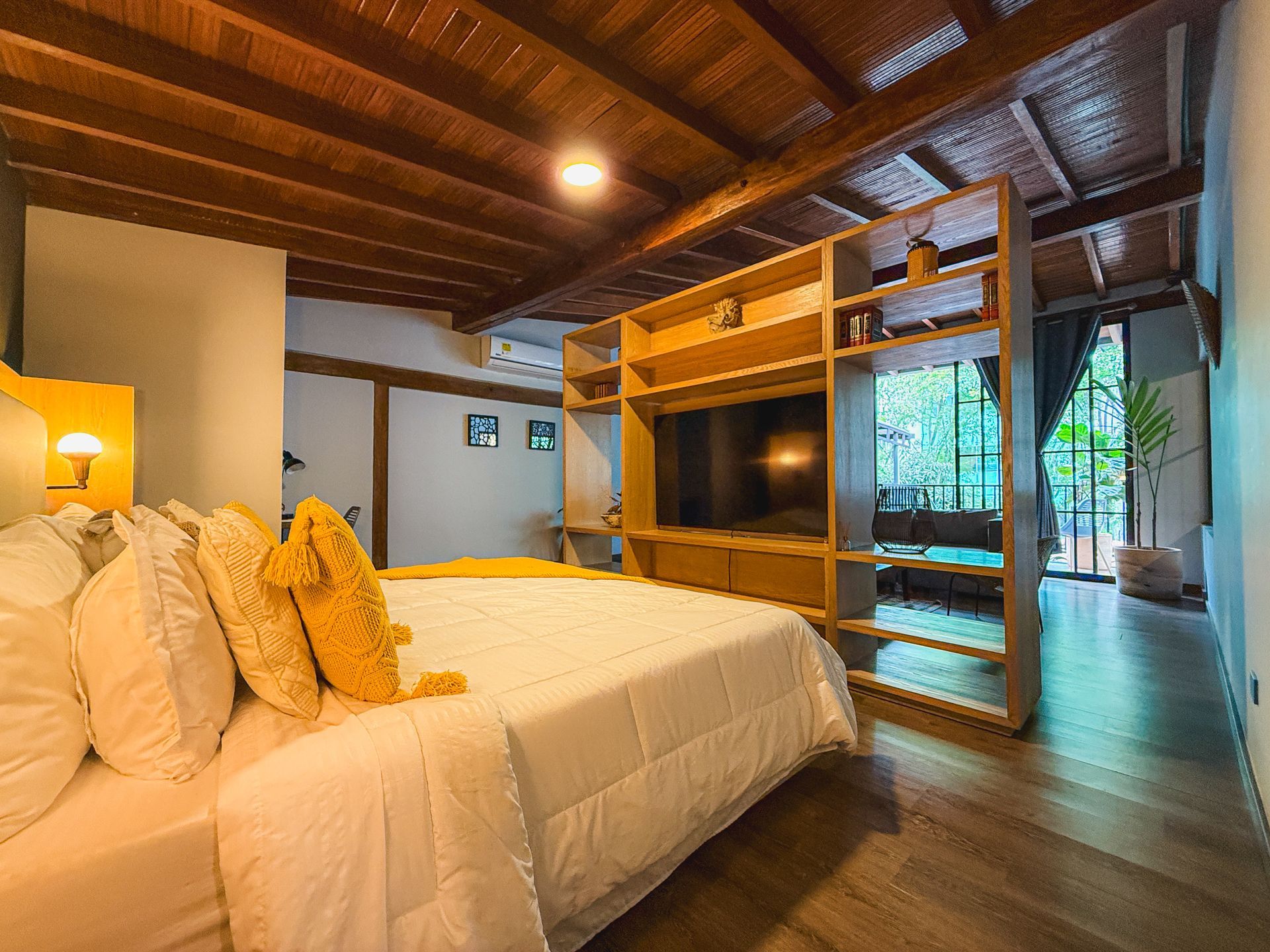 Dormitorio con techo de madera, estantería con TV y una cama con detalles en amarillo.