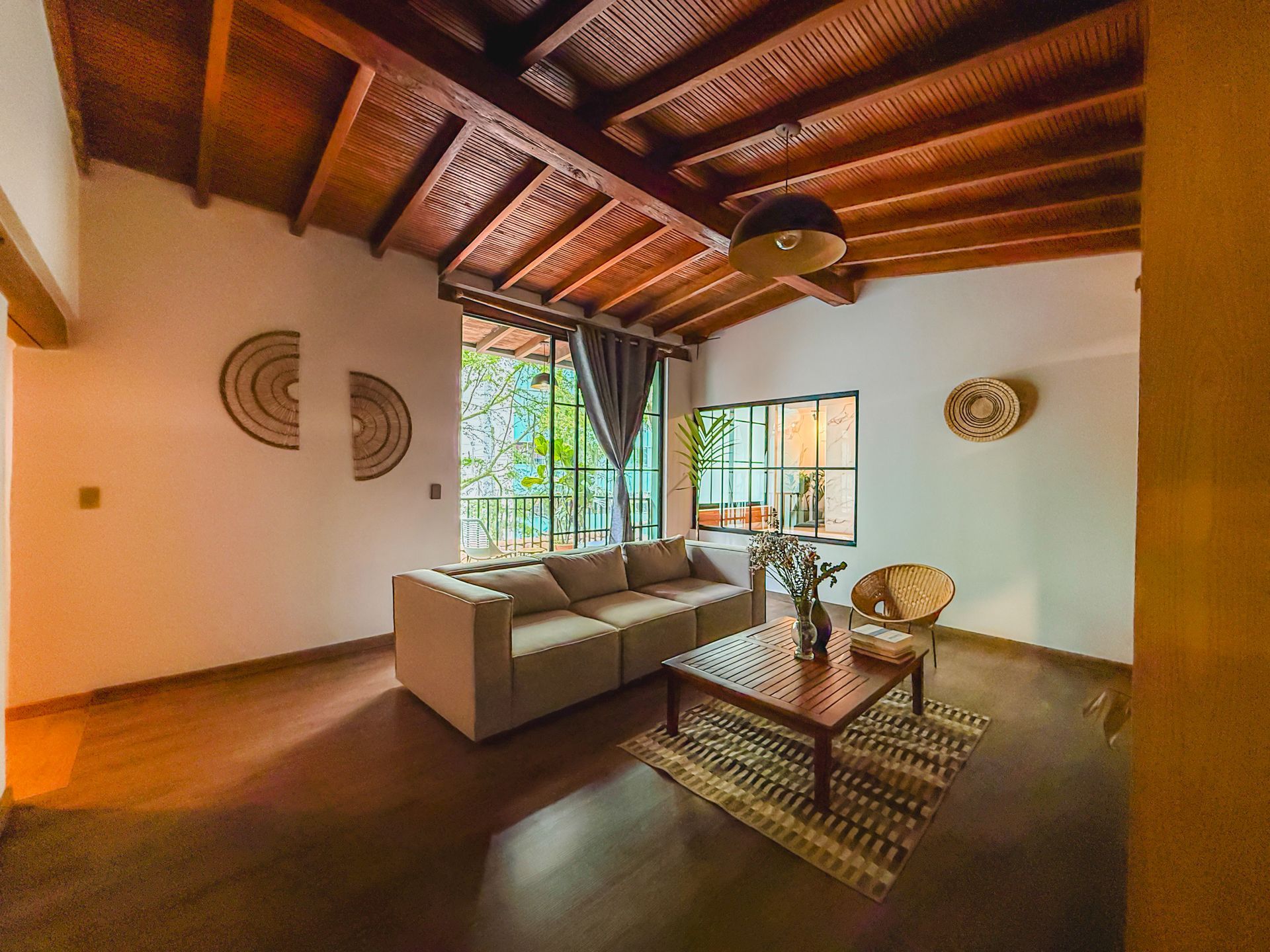 Sala de estar con techo de madera, sofá, mesa de café y grandes ventanales con vista a la vegetación.