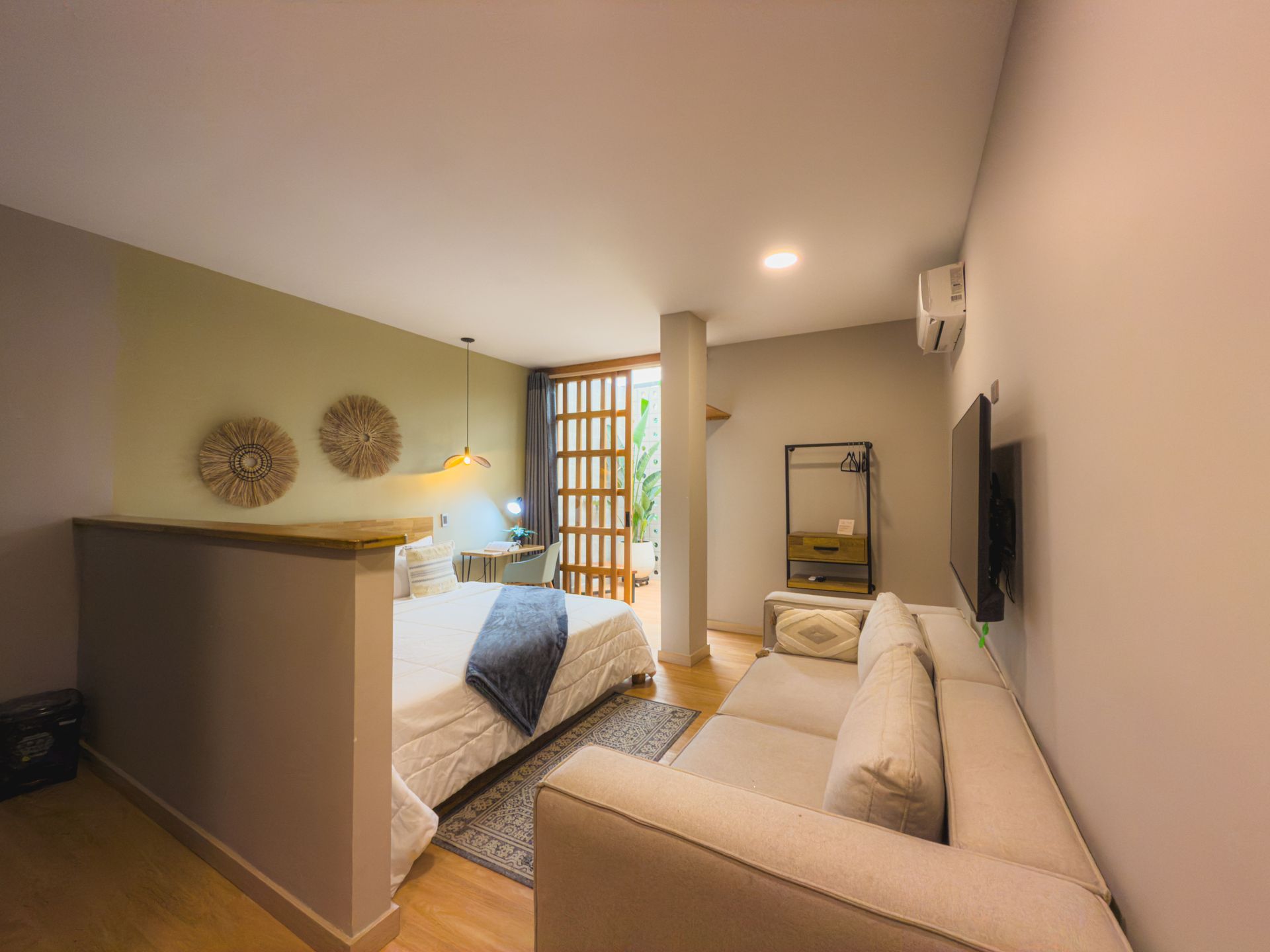 Dormitorio con cama, sofá y puertas abiertas a zona exterior; tonos neutros con detalles en madera.