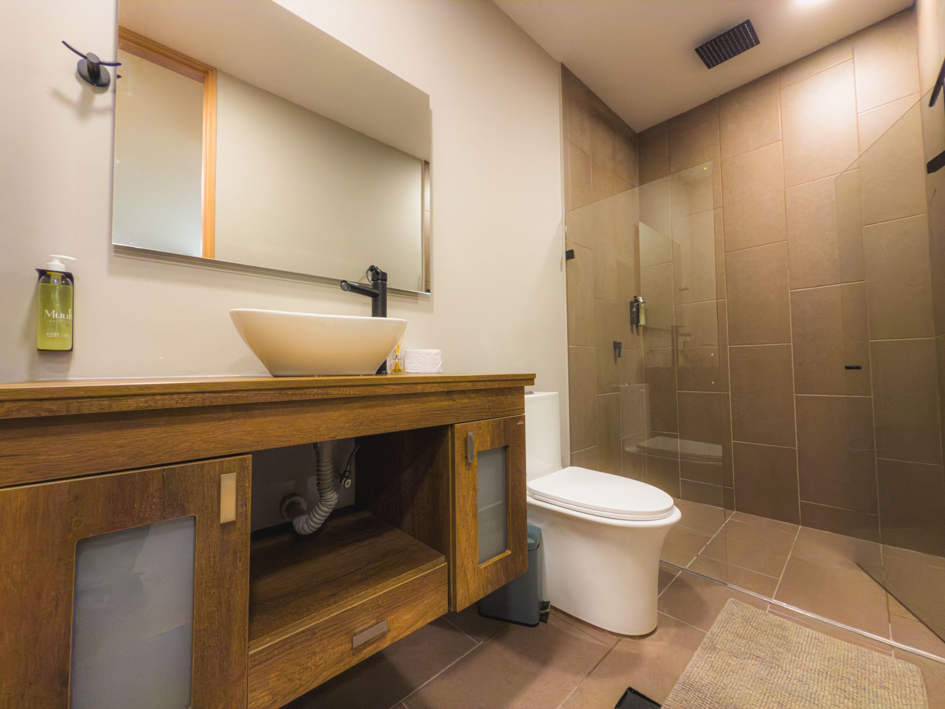 Baño con tocador de madera, lavabo blanco, inodoro y ducha de cristal.