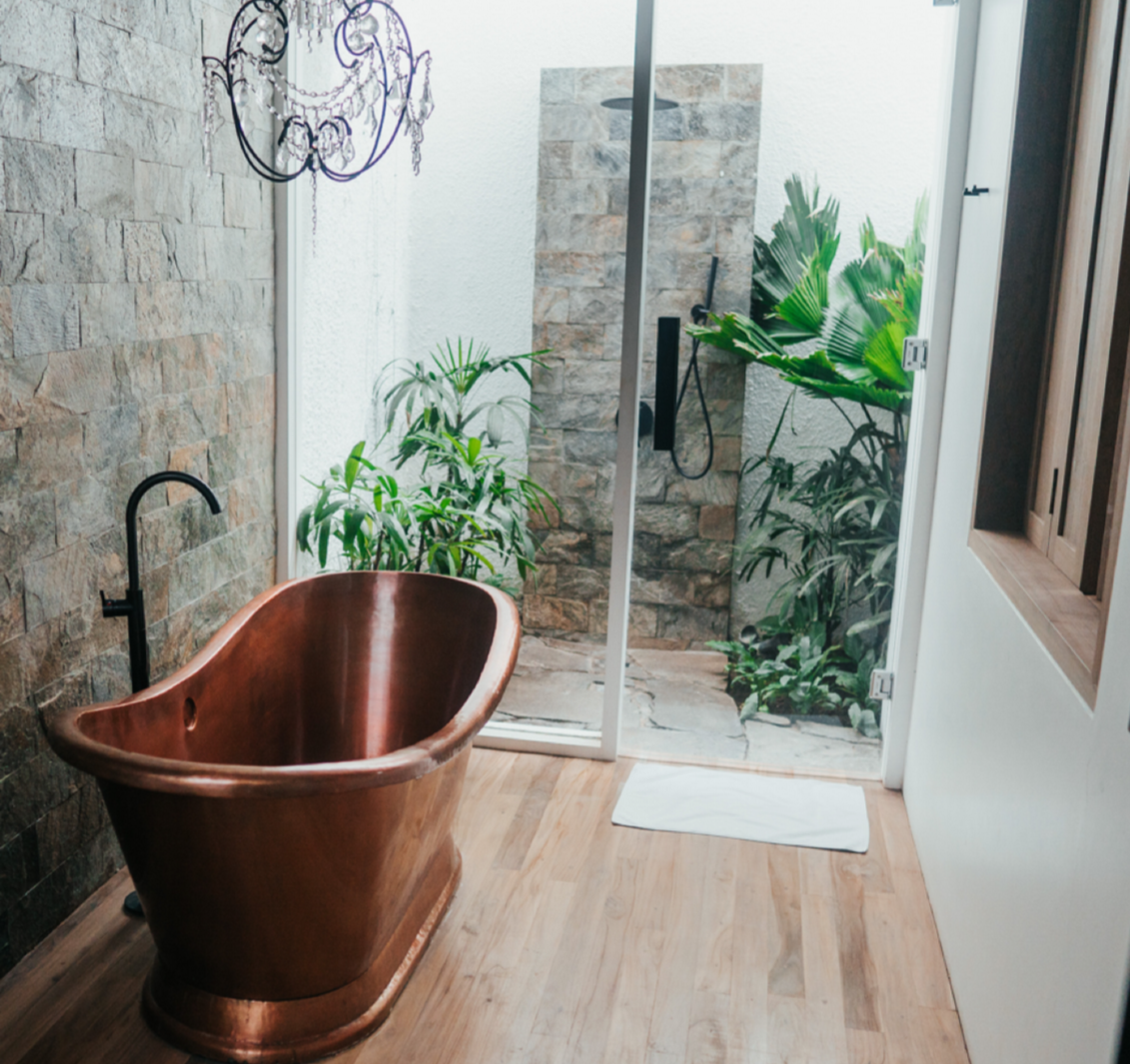 copper soaking tub in bathroom with nearby outdoor shower and floor to ceiling glass