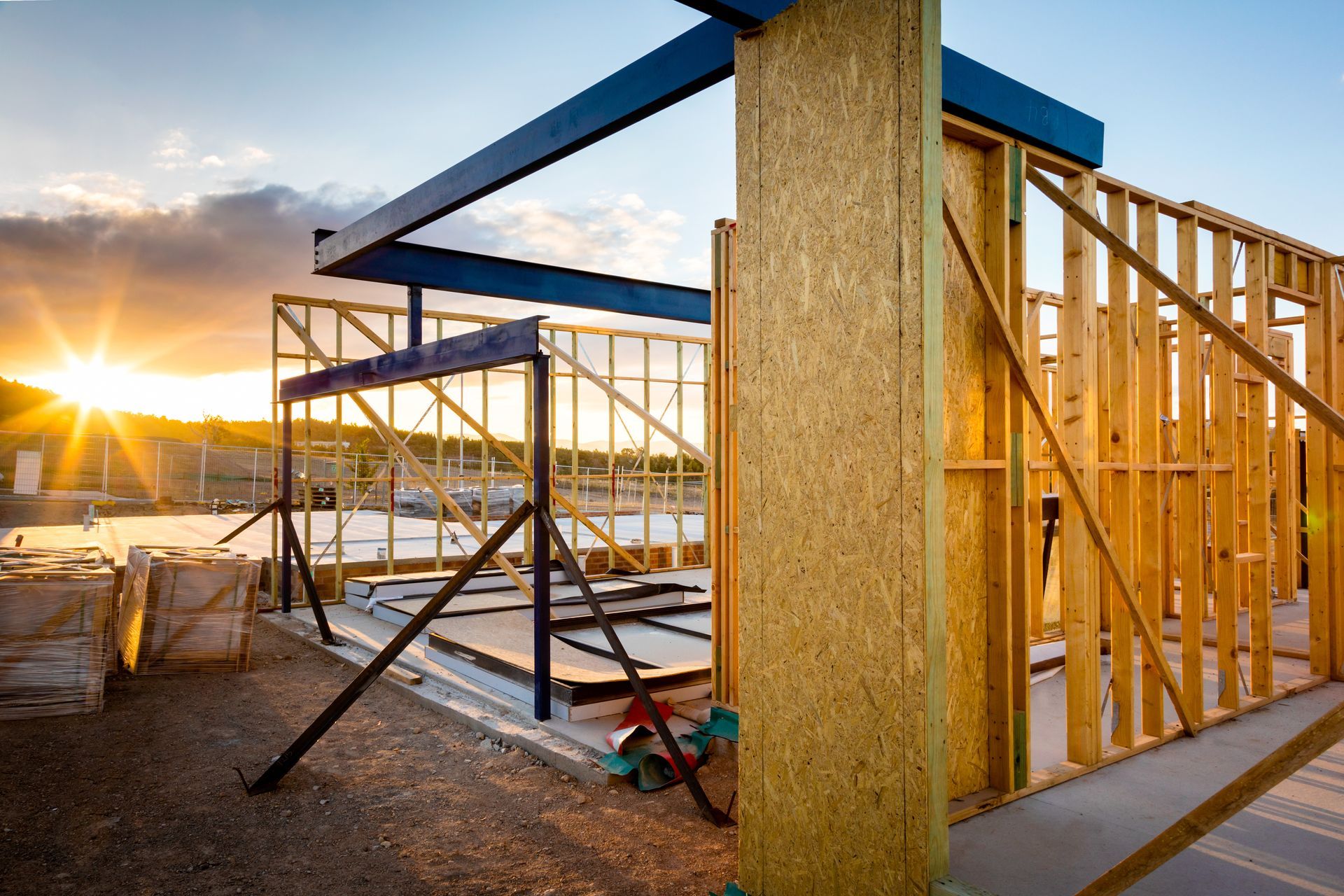 Construction site with wooden framing and a metal beam, at sunset.