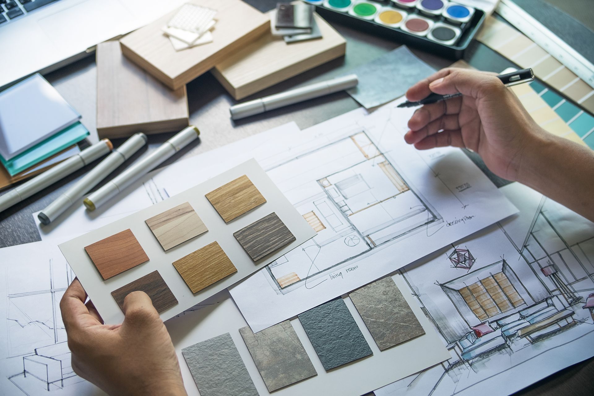 Hands holding wood samples, sketching on blueprints with paint and design tools.