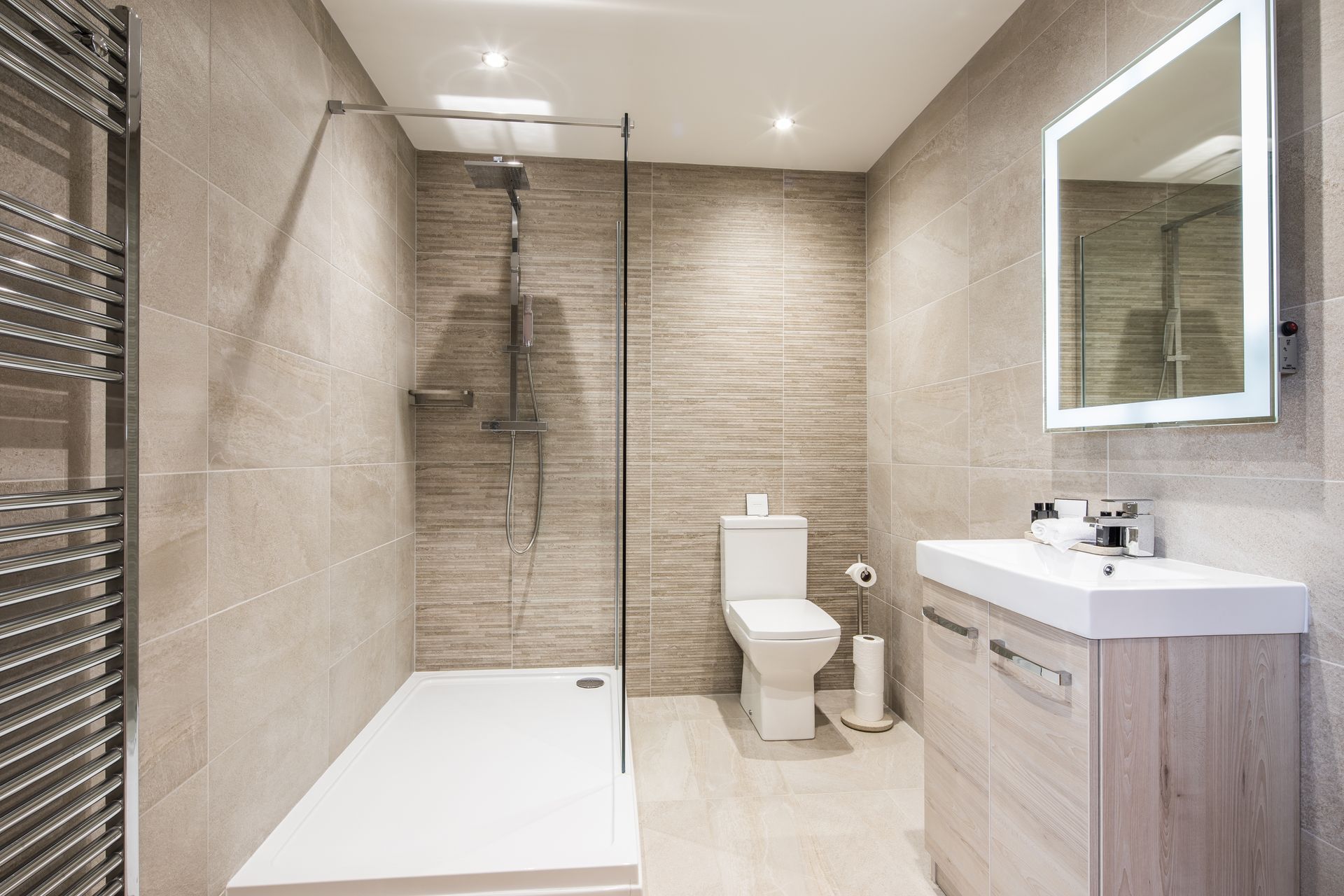 Modern bathroom with neutral-toned tiled walls and floor, shower, toilet, sink with illuminated mirror. Modern bathroom with neutral-toned tiled walls and floor, shower, toilet, sink with illuminated mirror.