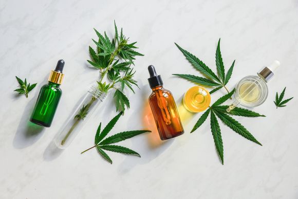 Various glass bottles with CBD oil, THC tincture and hemp leaves on a marble background