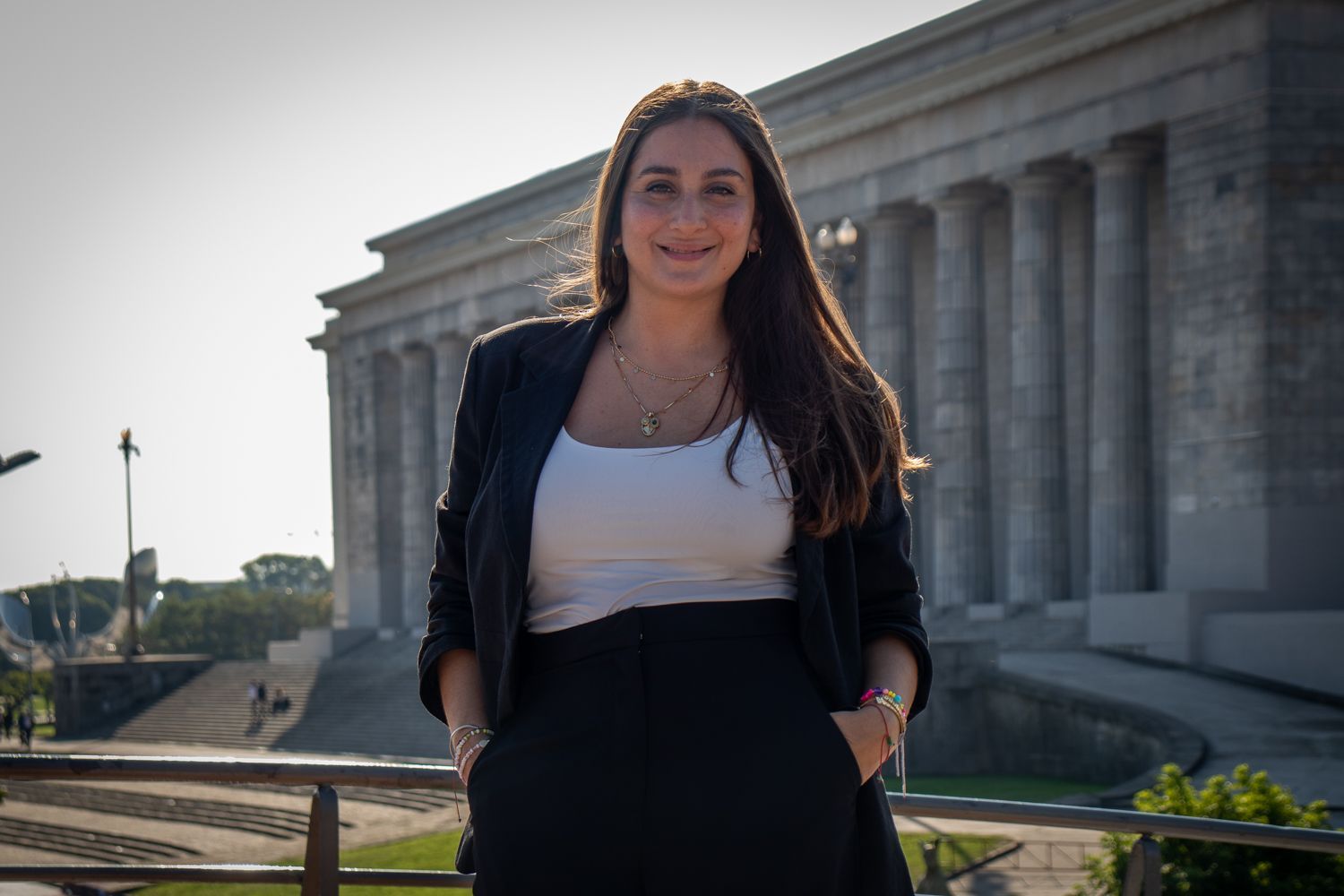 Mujer sonriente, de pie al aire libre con las manos en los bolsillos. Viste blazer negro
