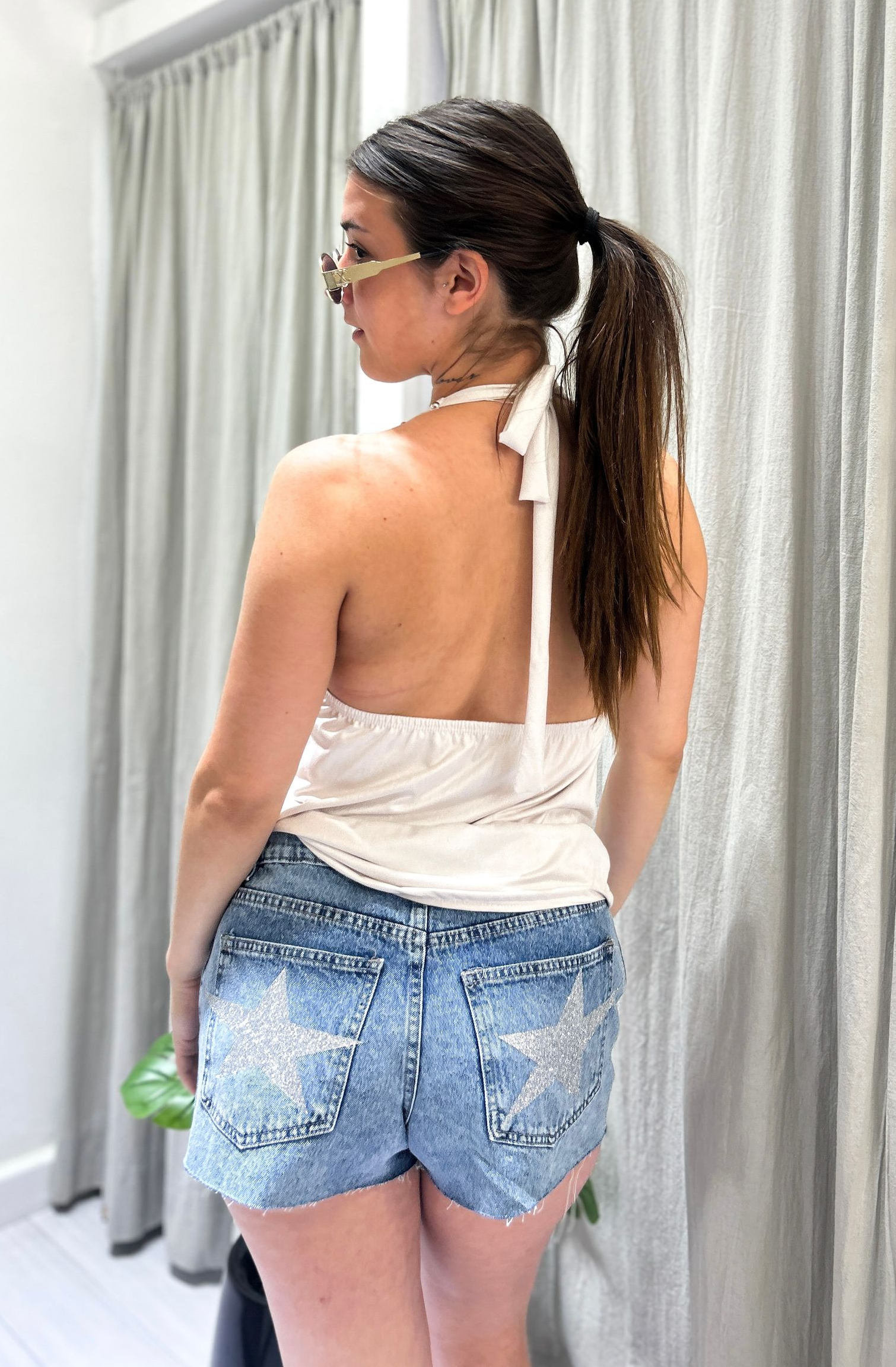 Mujer con top halter de color claro y shorts vaqueros, de pie en una tienda.