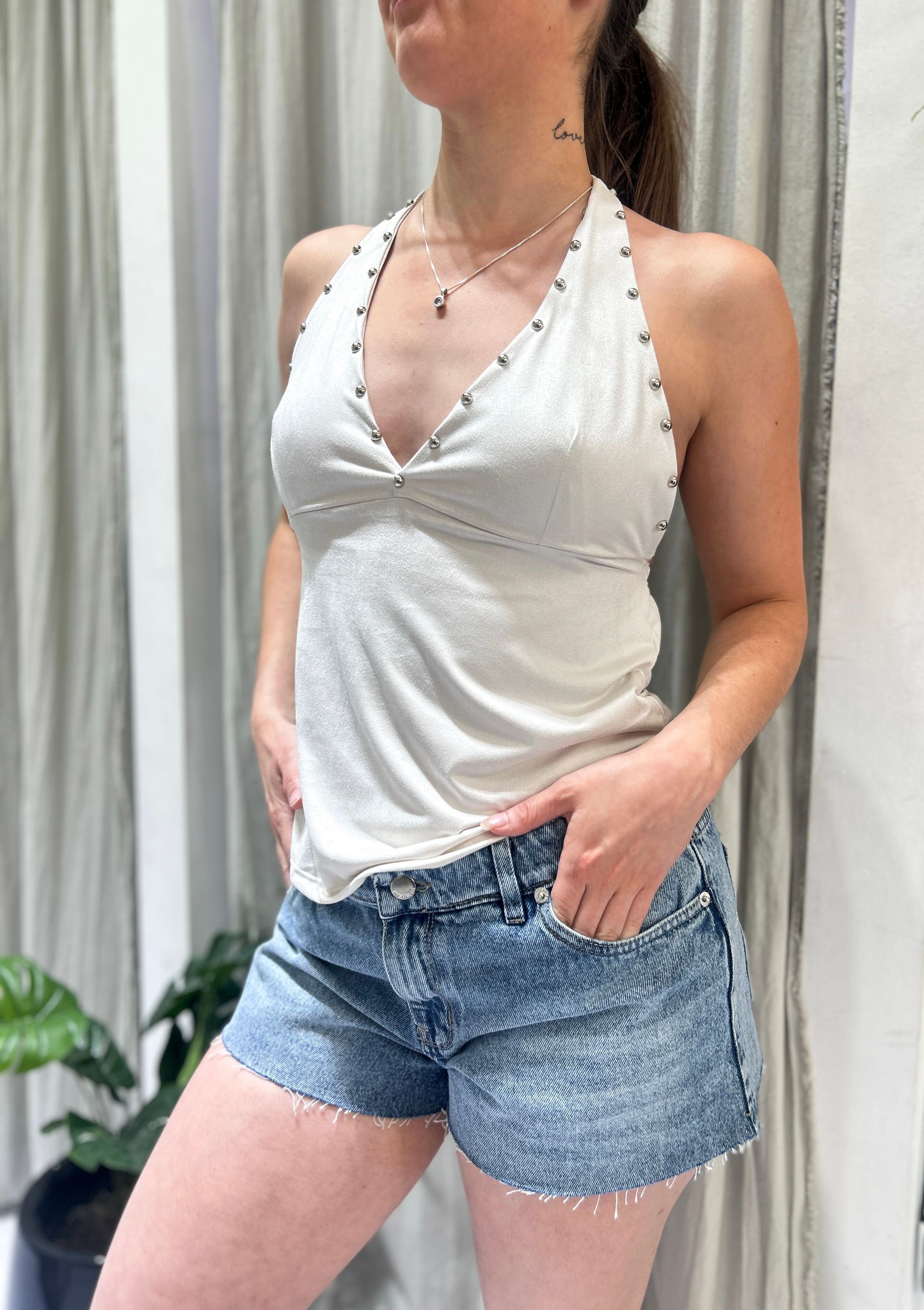 Mujer con top halter y shorts vaqueros, manos en los bolsillos, posando en interiores.