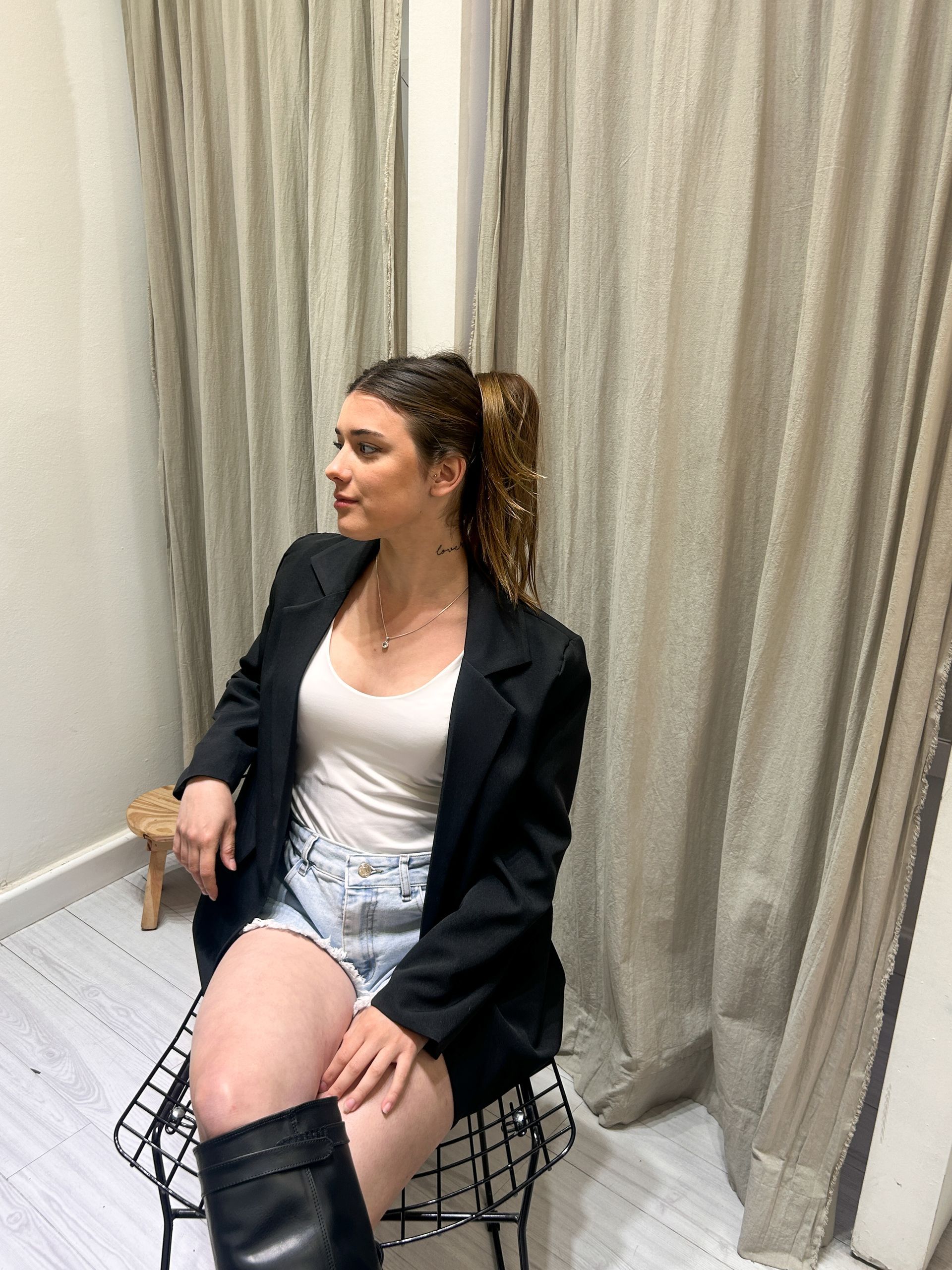 Mujer vestida con blazer negro, blusa blanca, shorts de mezclilla y botas.