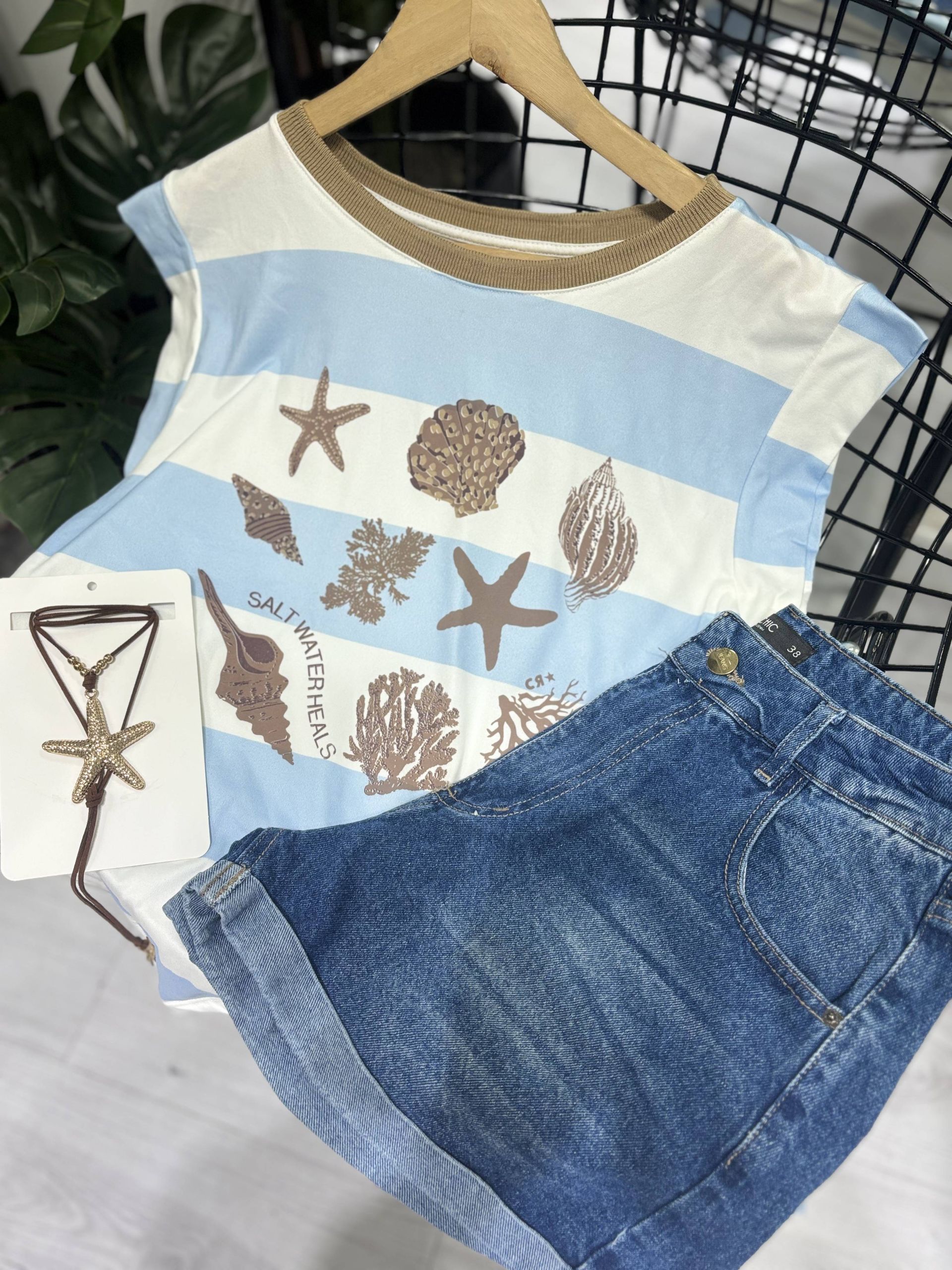 Camisa azul a rayas con conchas marinas, pantalones cortos vaqueros y collar.
