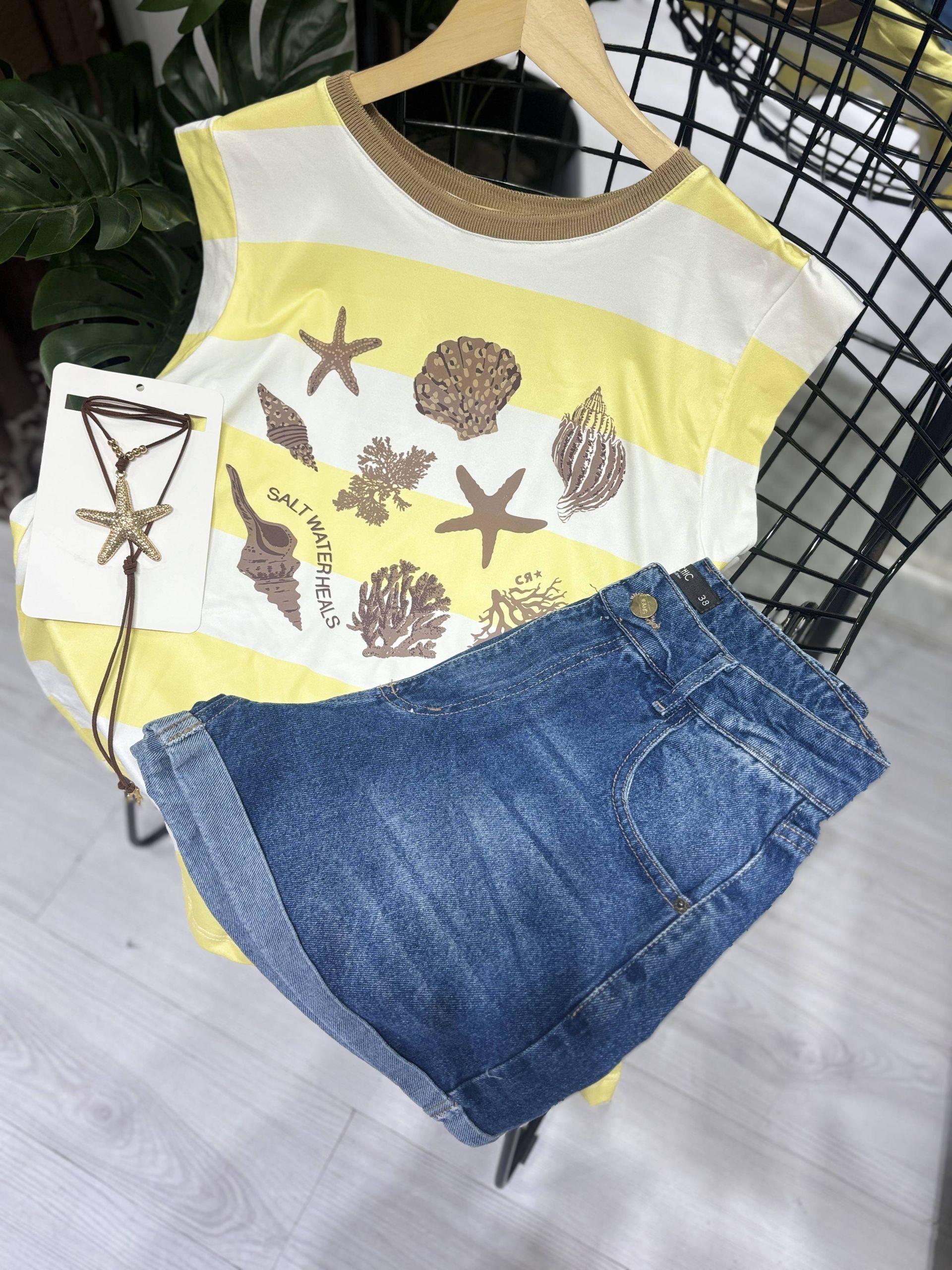 Camisa azul a rayas con conchas marinas, pantalones cortos vaqueros y collar.