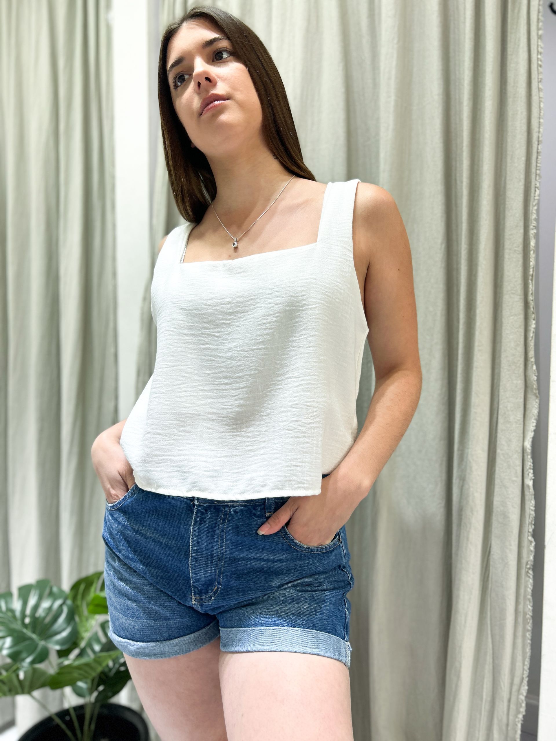 Mujer con blusa blanca y shorts vaqueros, manos en los bolsillos, mirando a la cámara.