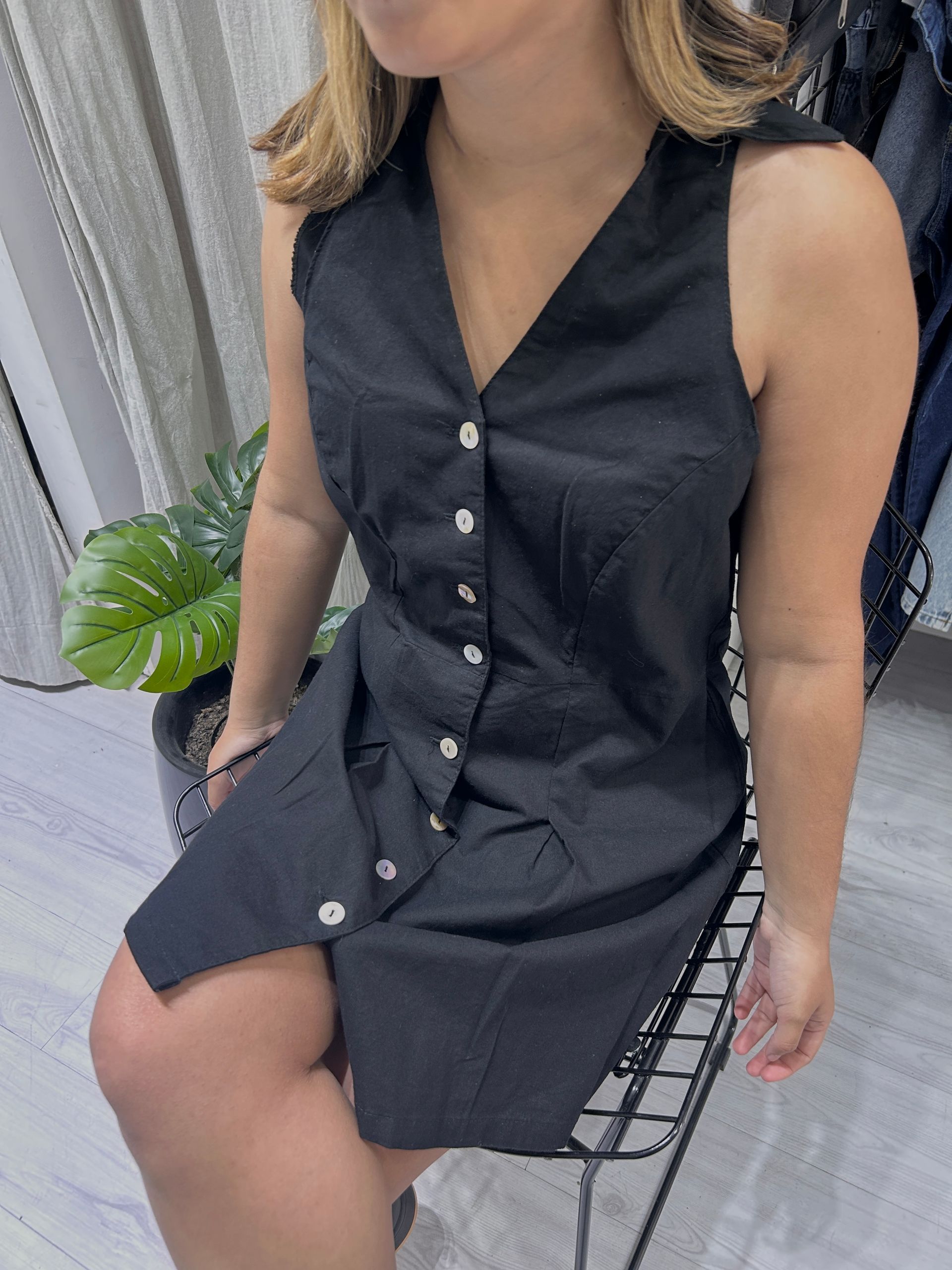 Mujer sentada, vestida con un vestido negro sin mangas con botones.