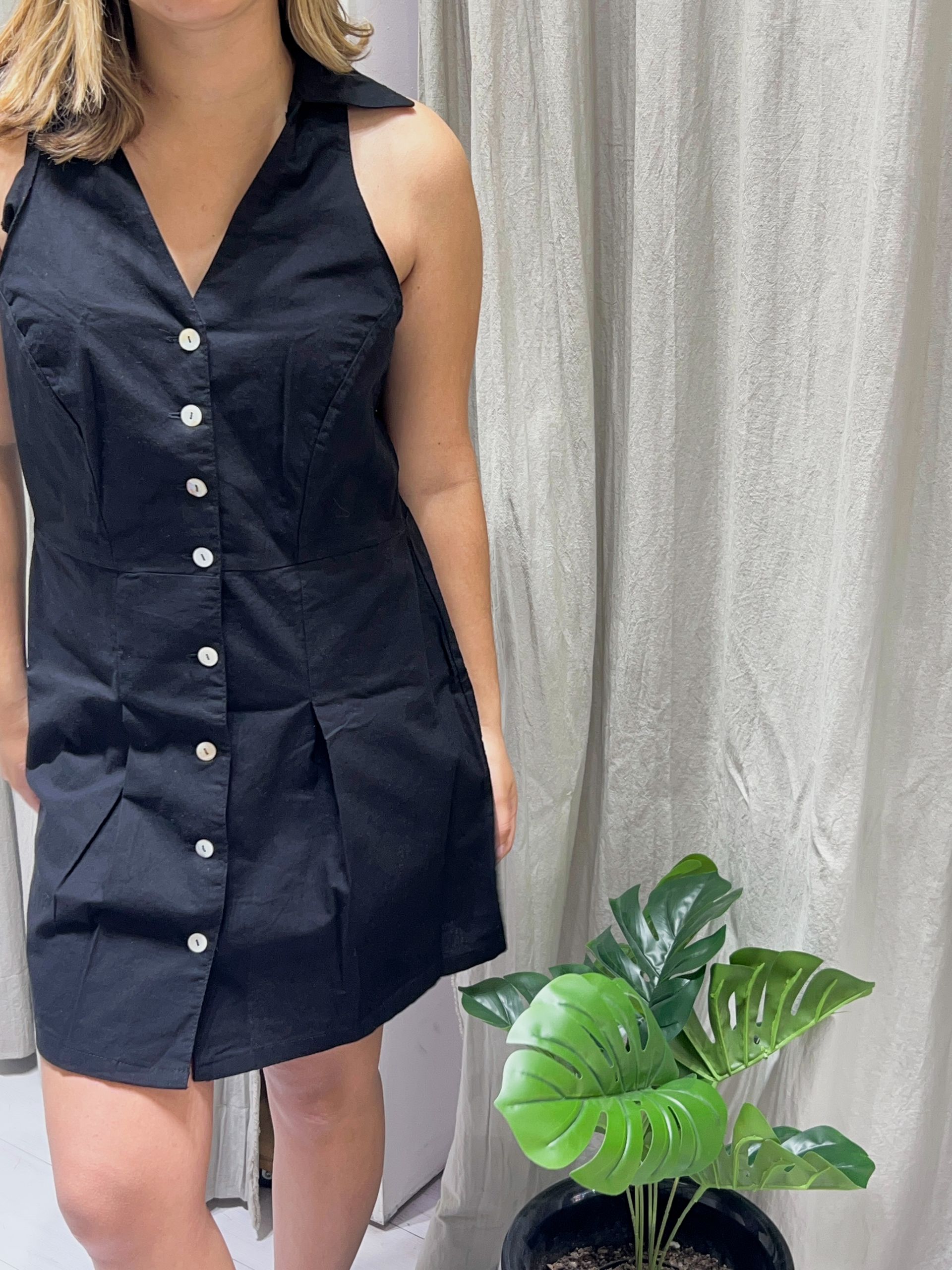 Mujer sentada, vestida con un vestido negro sin mangas con botones.